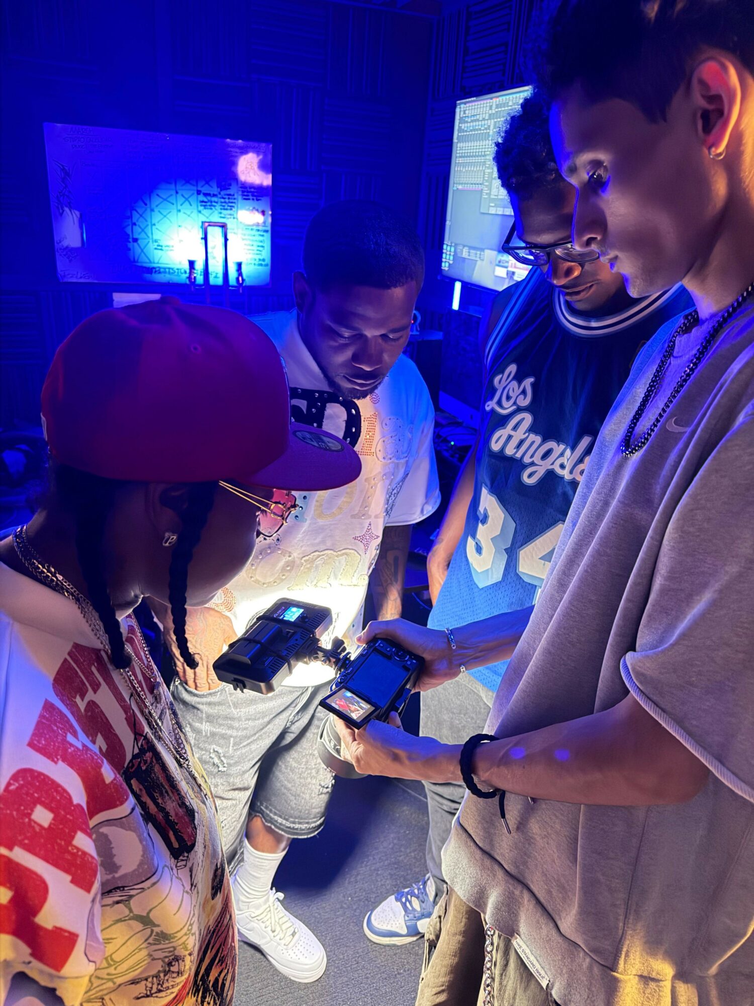 Four young people in a dark room with screens, looking at handheld devices, illuminated by screen light.