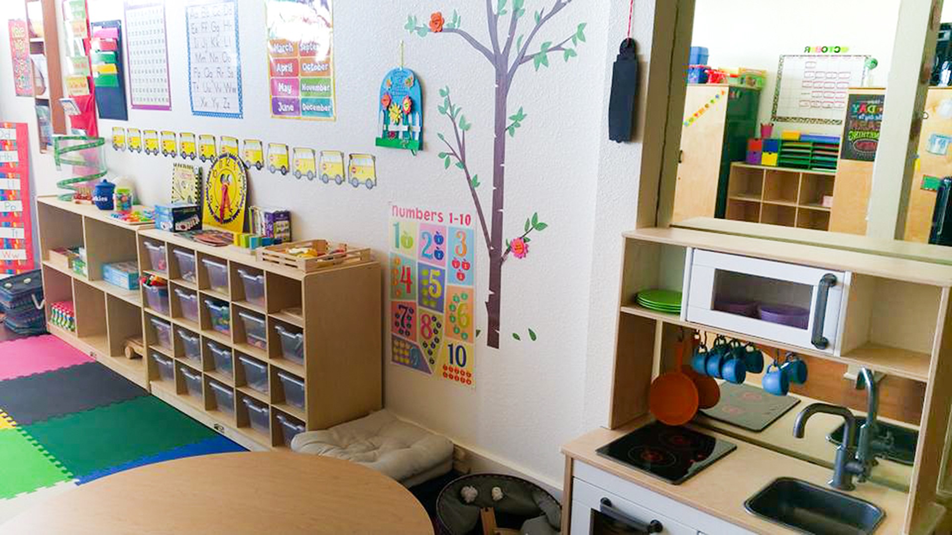 Classroom with shelves, colorful posters, and a tree illustration on the wall.