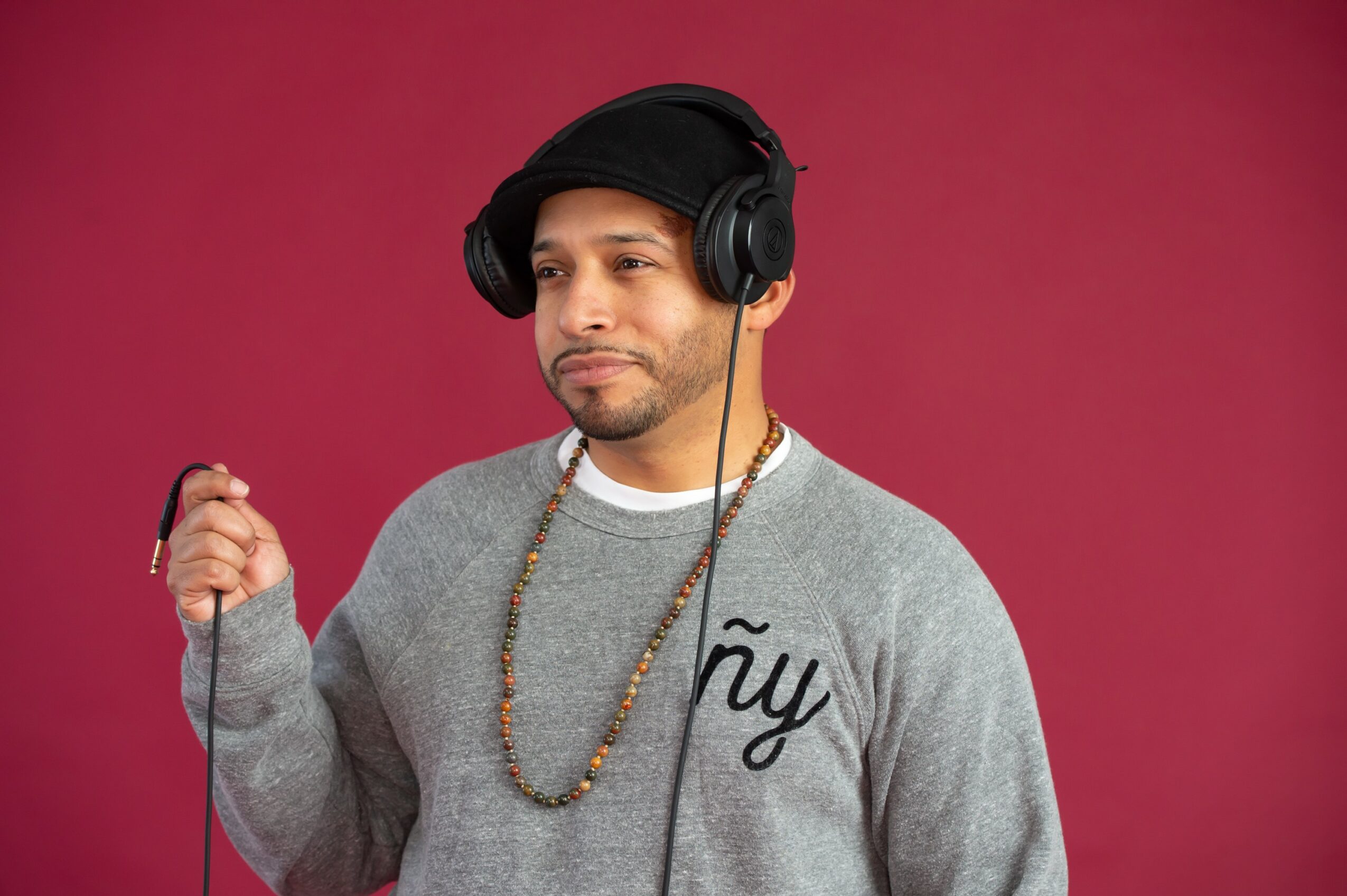 Man wearing headphones and a gray sweatshirt with text, holding a cable, against a pink background.