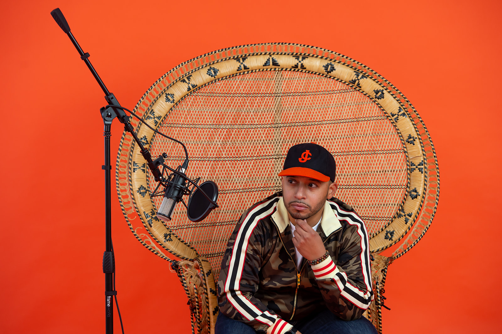 Person sitting in a wicker chair with a microphone and stand, against an orange background.