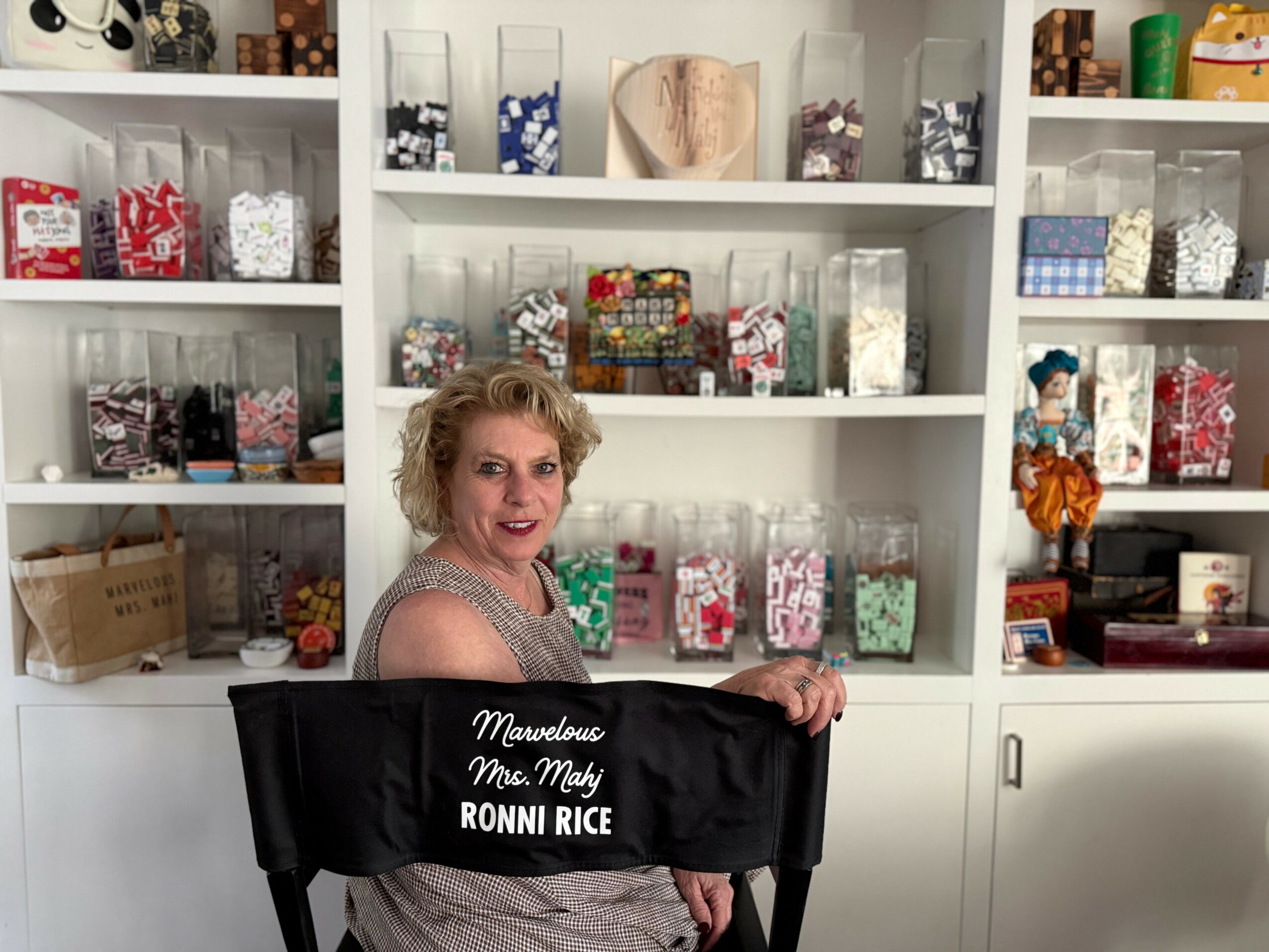 Woman with short curly hair smiling in front of shelves filled with colorful gift boxes and decorations.