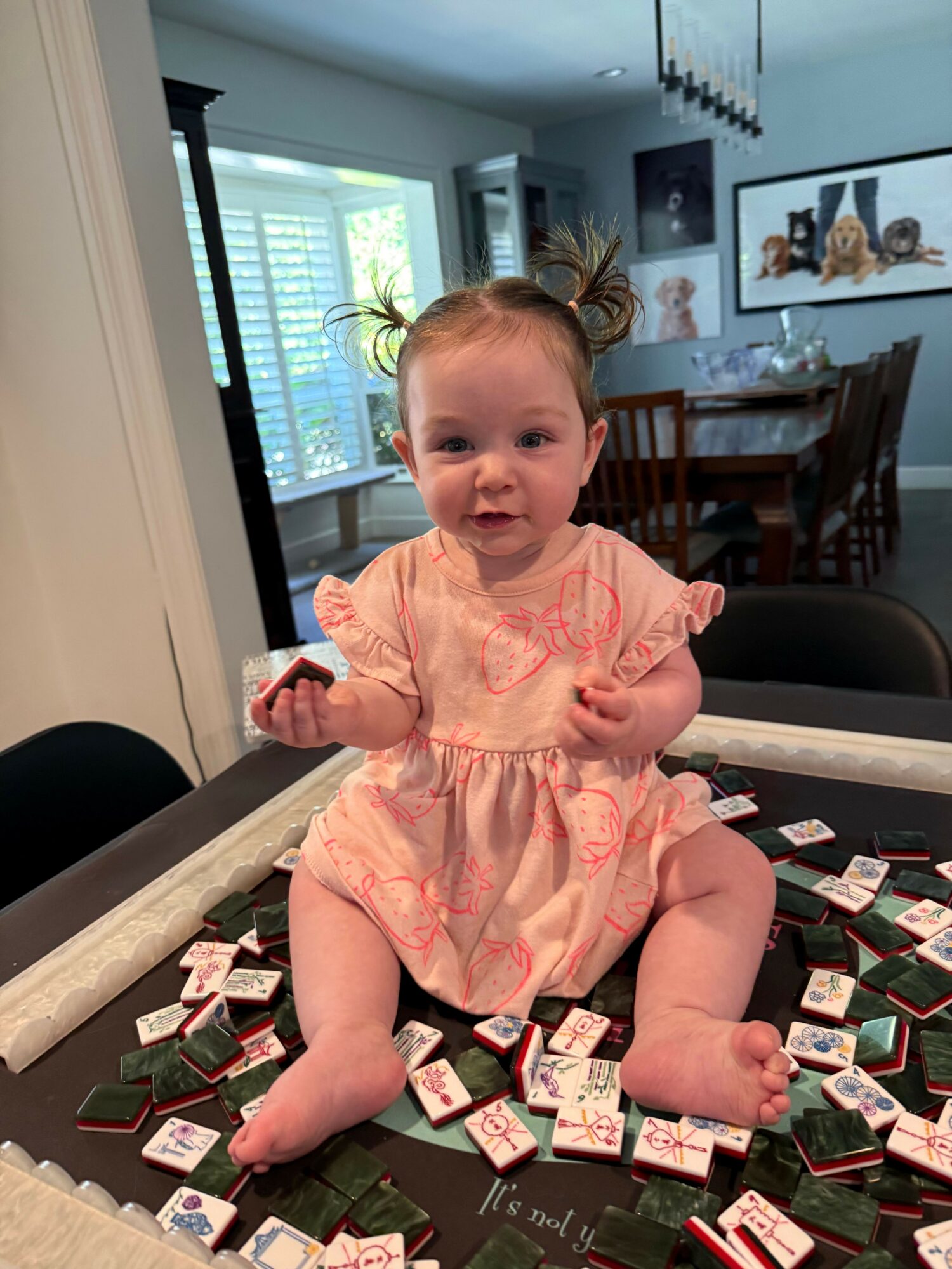 Baby girl sitting on a table surrounded by scattered small boxes, smiling and holding a box in her hand.