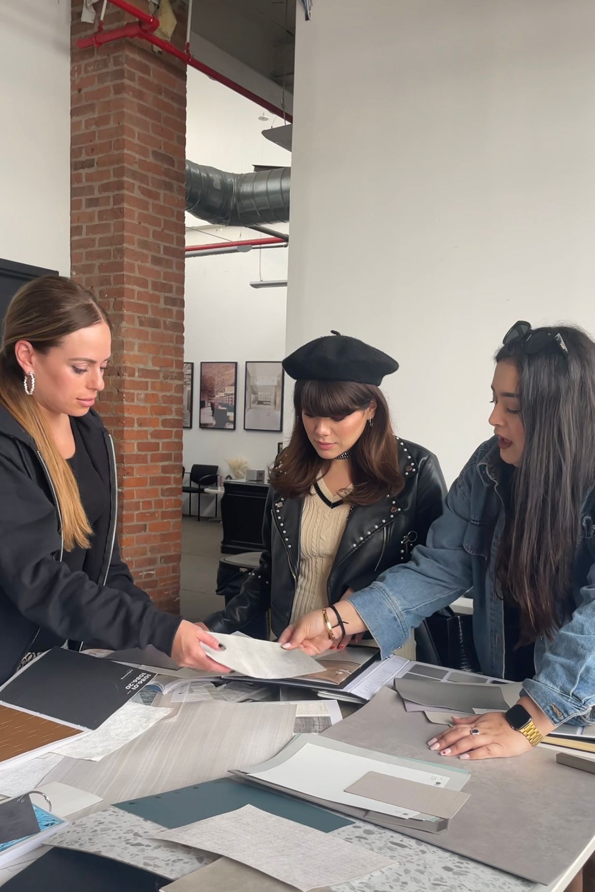 Three women standing around a table with papers and documents in an indoor setting.