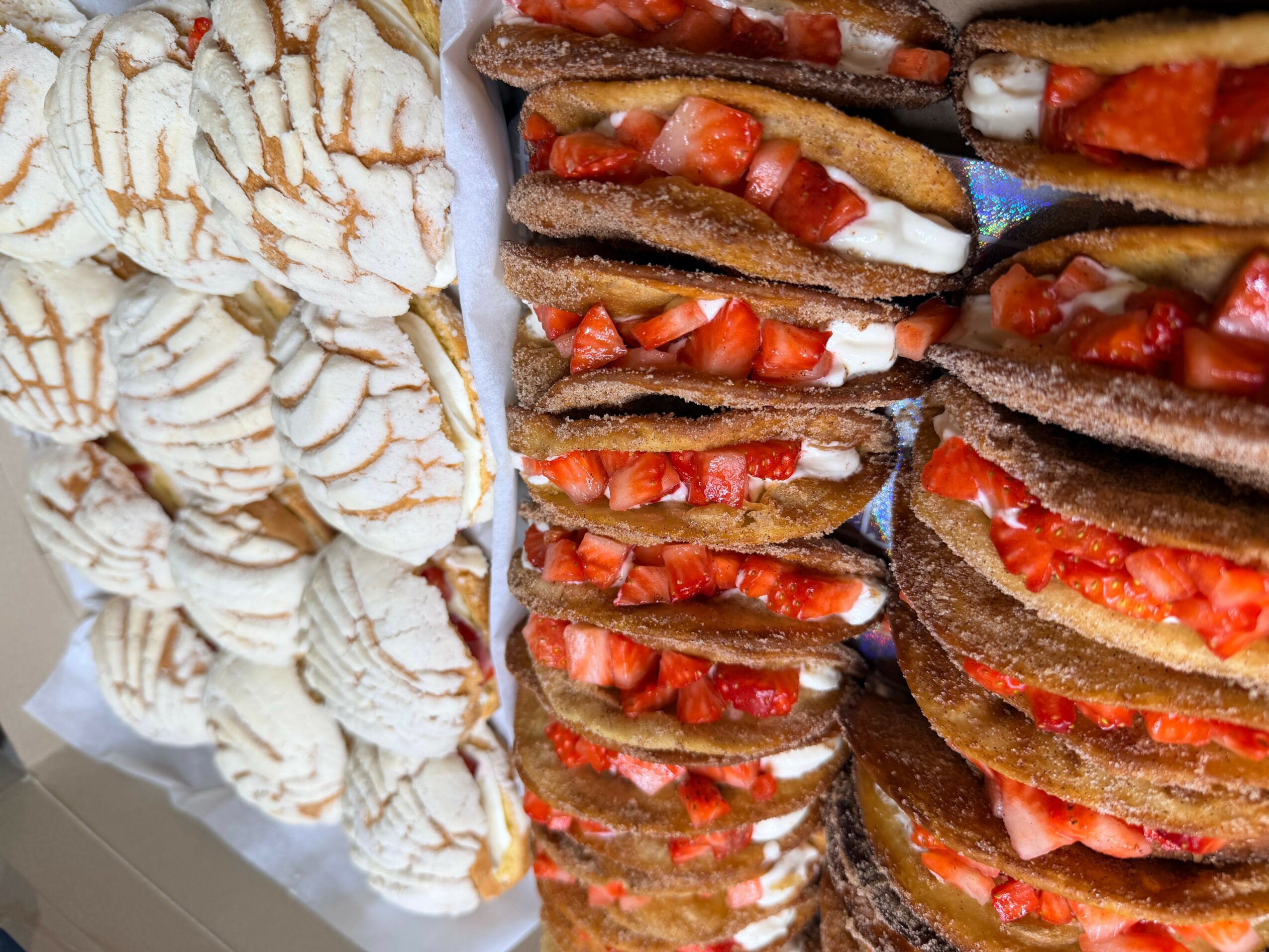 Stacked chocolate crepes with strawberries and cream next to a pile of sliced bananas with syrup.