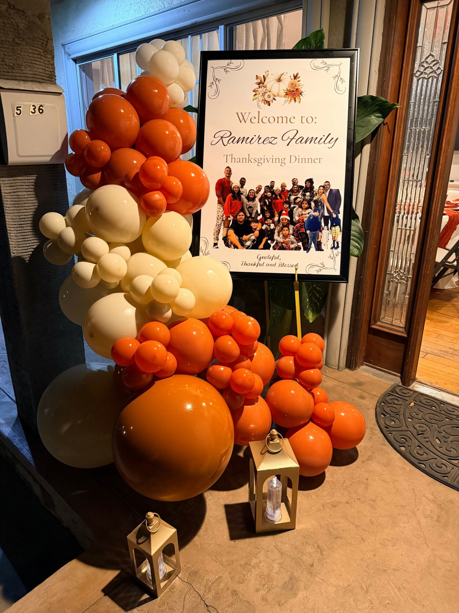 Decorative arrangement of orange and white balloons with a welcome sign for Ramere Family Thanksgiving Dinner, lanterns, and a door mat.