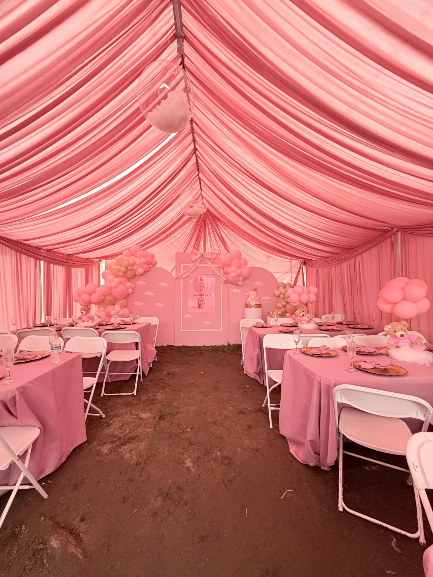 Pink decorated event tent with draped fabric ceiling, round tables with pink tablecloths, and white chairs.