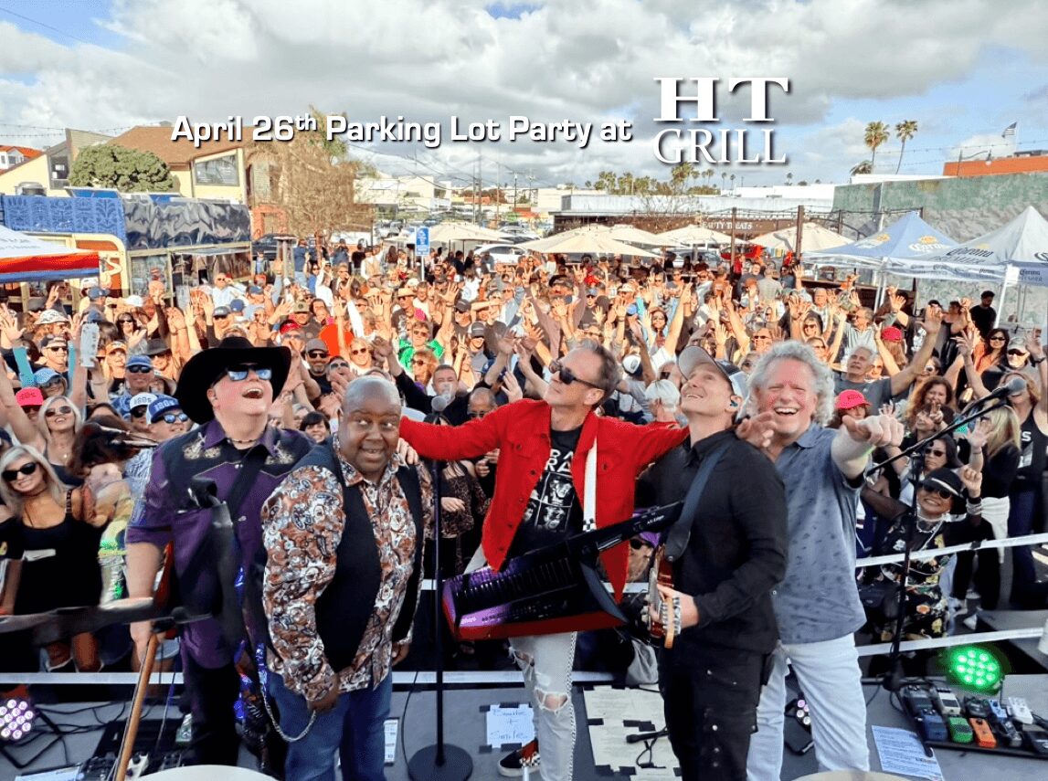 Four people on stage with a large crowd in the background at an outdoor event.