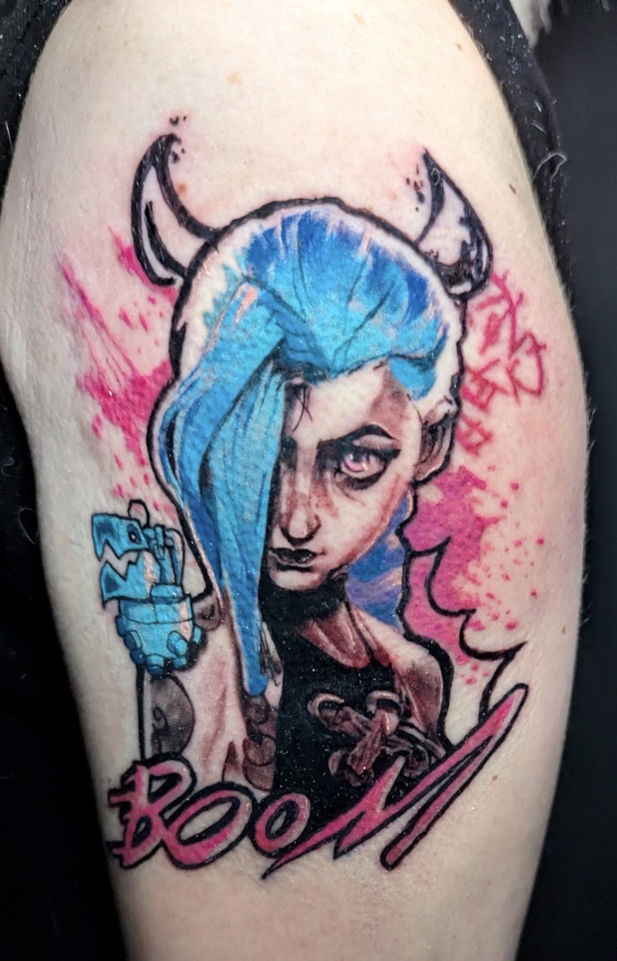 Tattoo of a woman with blue hair, holding a gun, with pink and black accents and the word 'BOOM'.