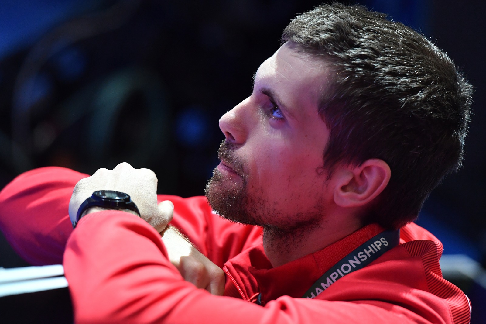 Man in red jacket looking to the side, with a dark background.