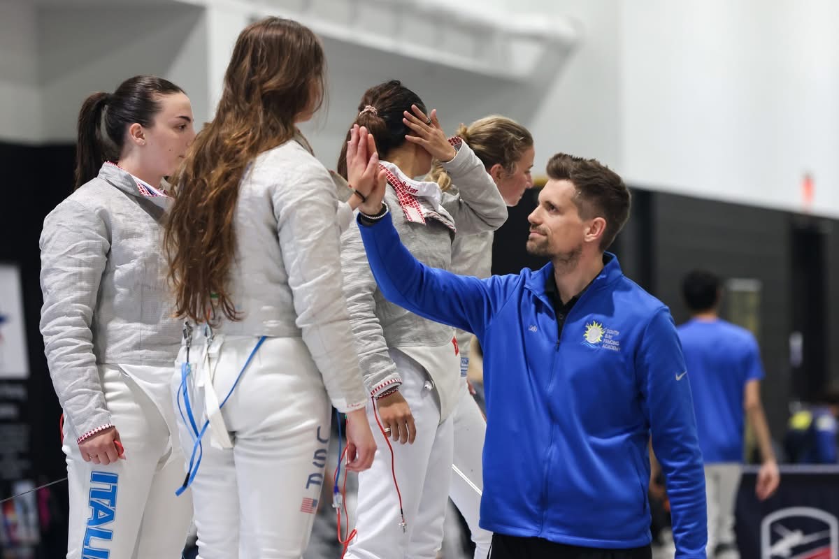 Male coach high-fives female athlete in a white judo uniform during a ceremony, with other athletes nearby.