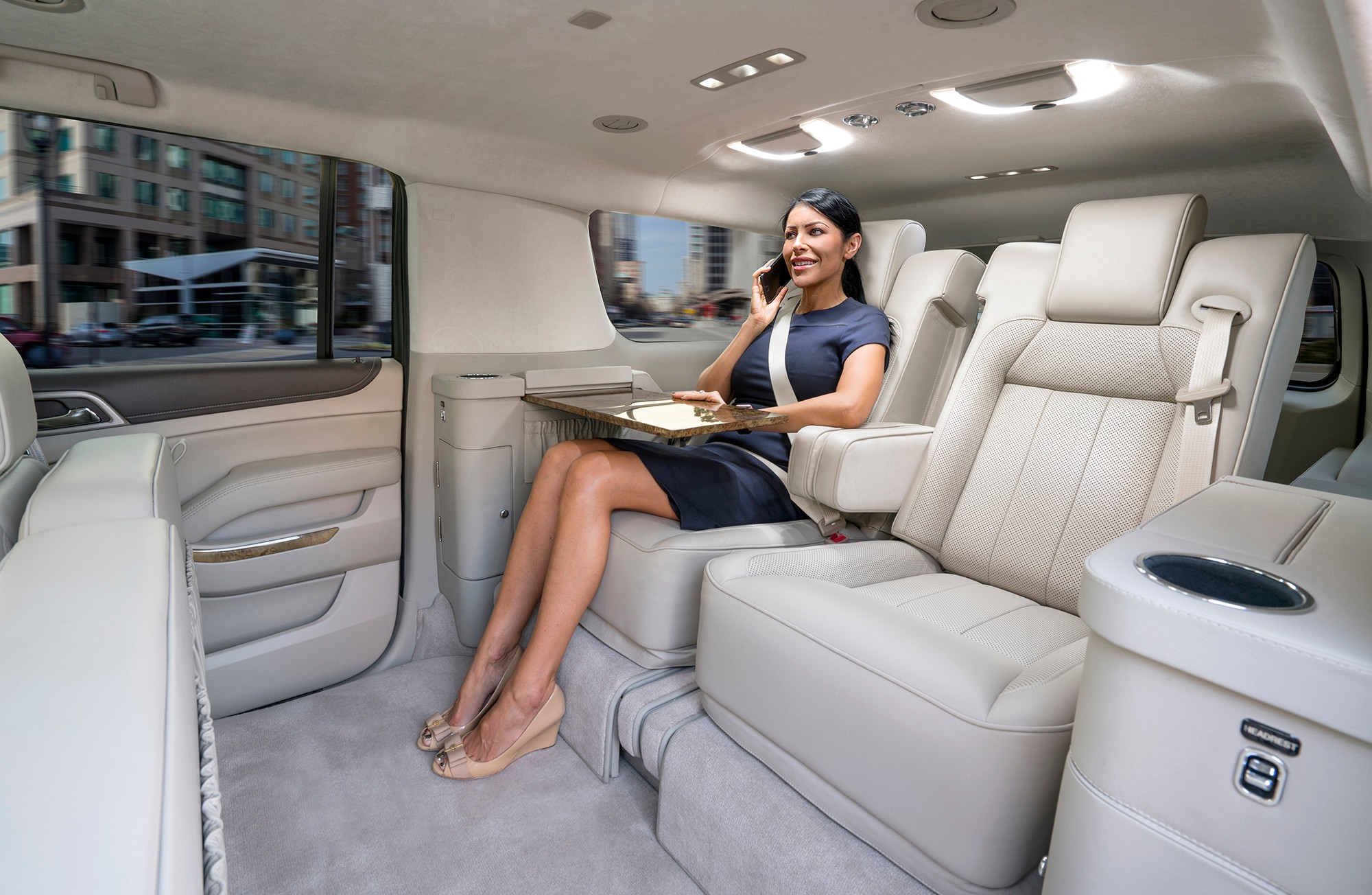 Woman sitting in luxury vehicle interior, smiling, holding a tablet, with cityscape visible through window.