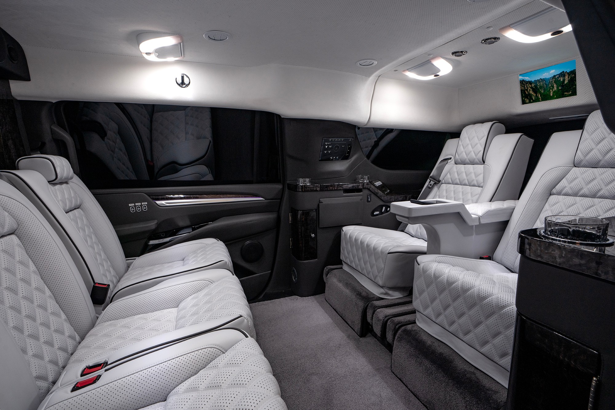 Interior of a luxury vehicle with white leather seats, armrests, and overhead lighting, viewed from the back.