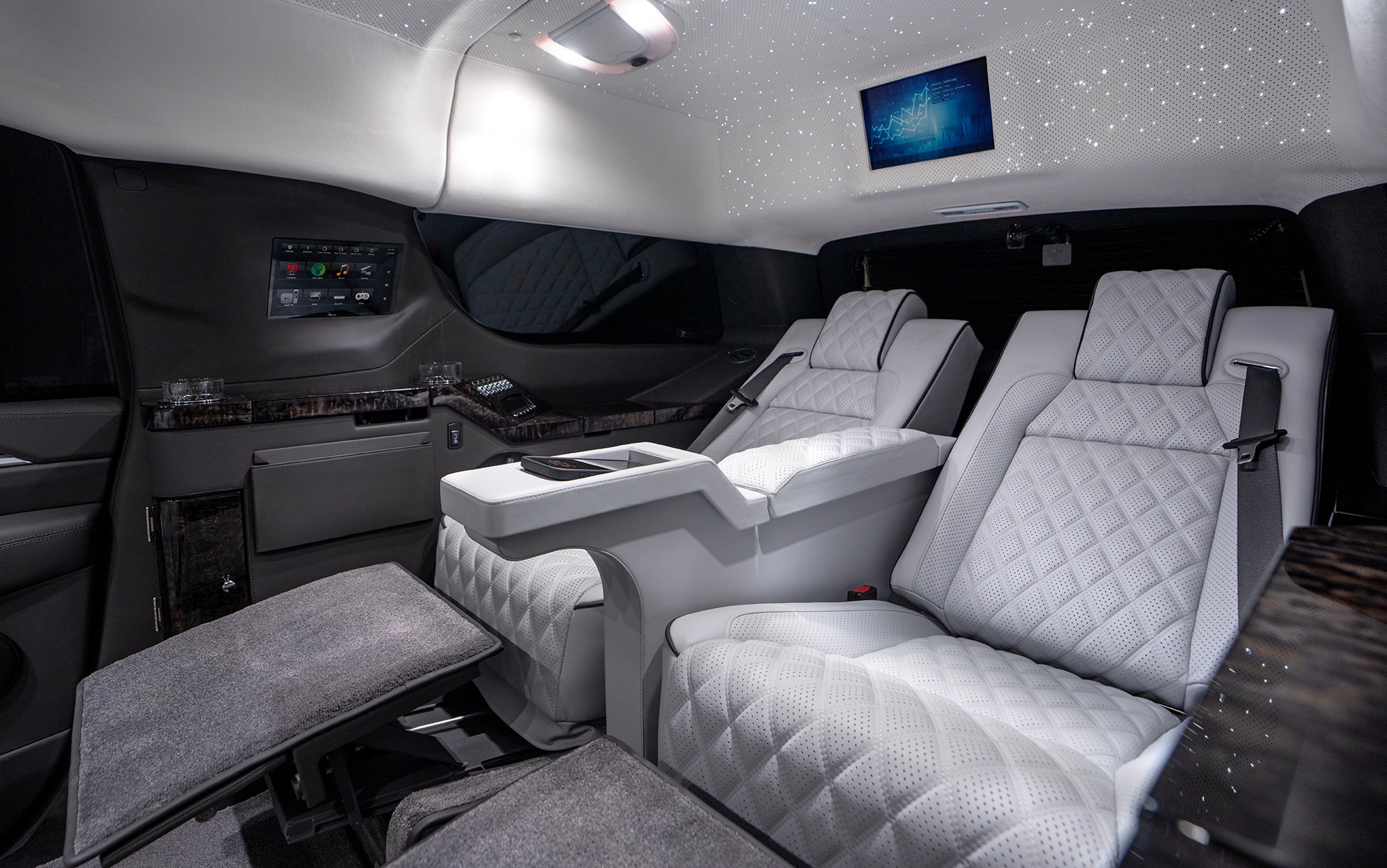 Luxury airplane interior with two white quilted seats, a control panel, and a starry ceiling display.