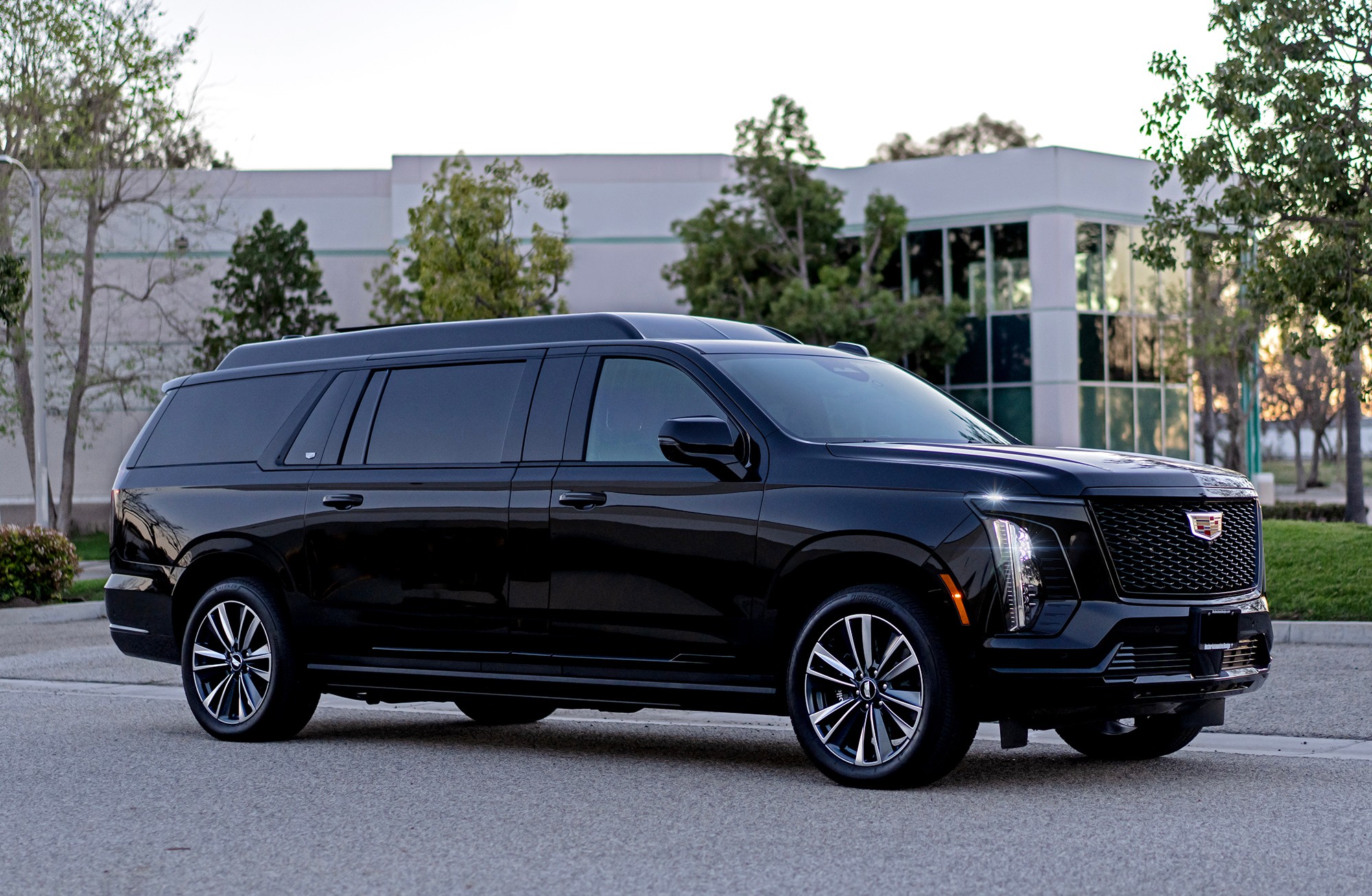 Black SUV parked on street with modern building and trees in background.