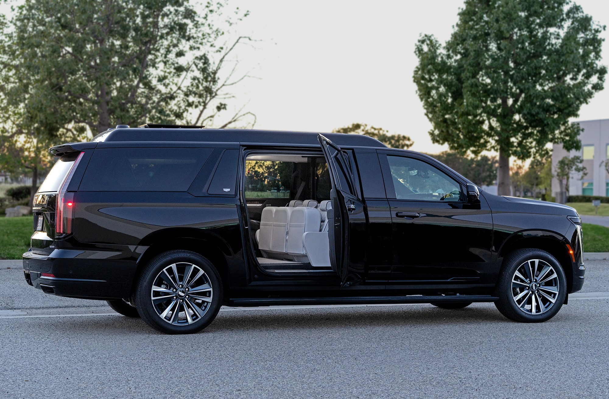 Black SUV with open sliding door showing white interior seats parked on street with trees in background.