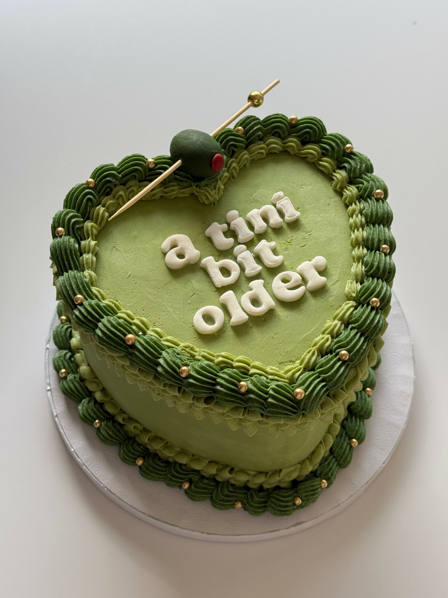 Heart-shaped cake with green icing and decorative borders, with the message 'a time but older' written on top.