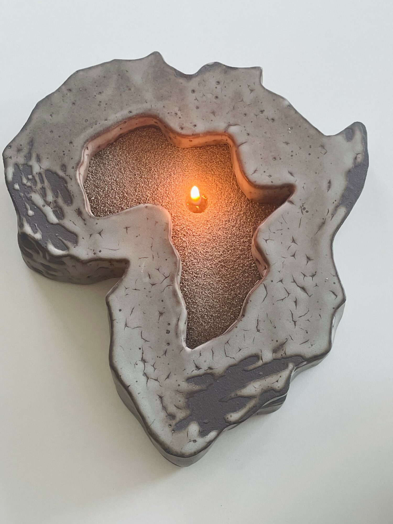 Candle holder shaped like the African continent with a lit candle inside, placed on a white surface.