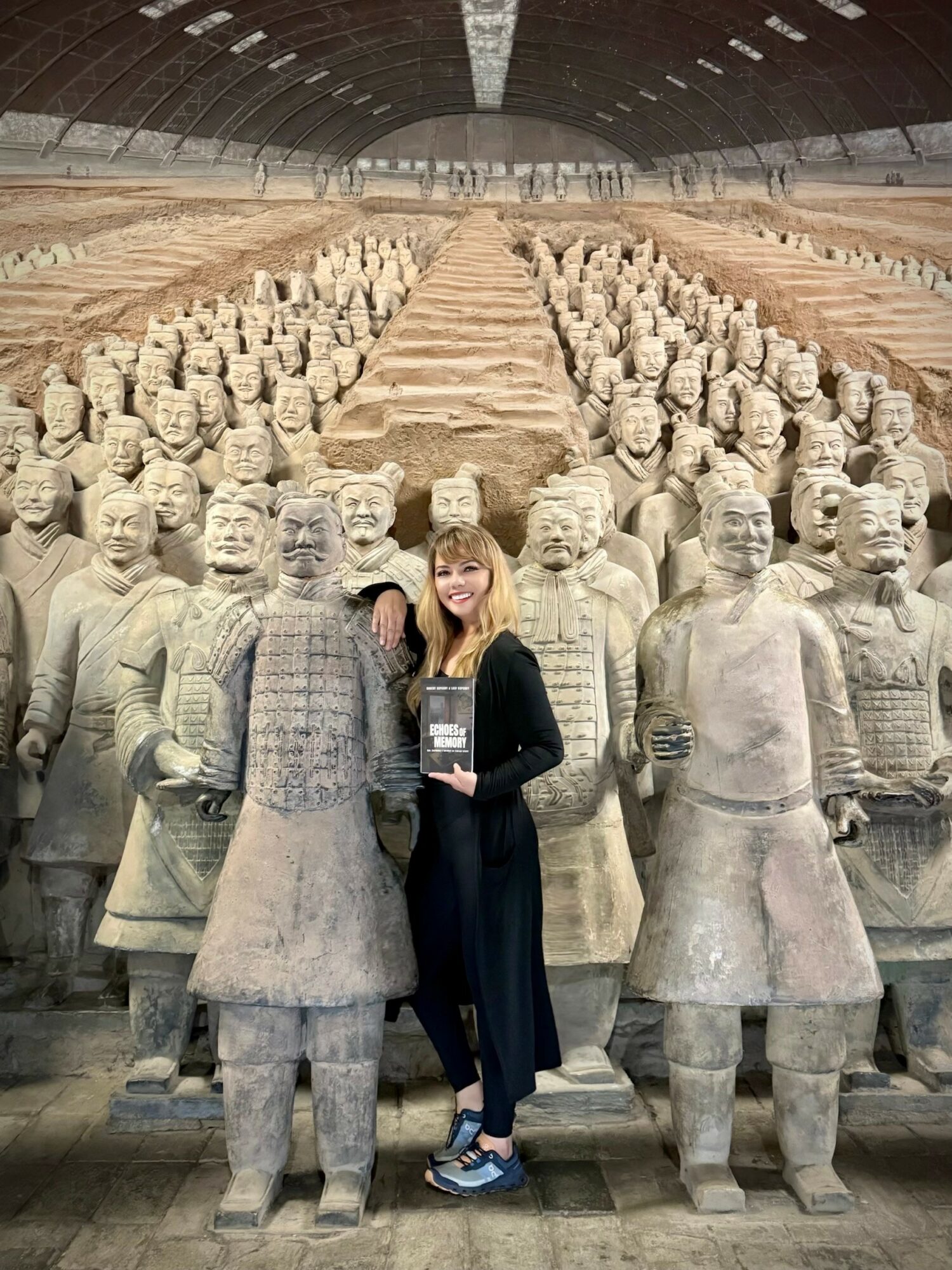 Woman standing among large terracotta warrior statues inside a spacious hall.