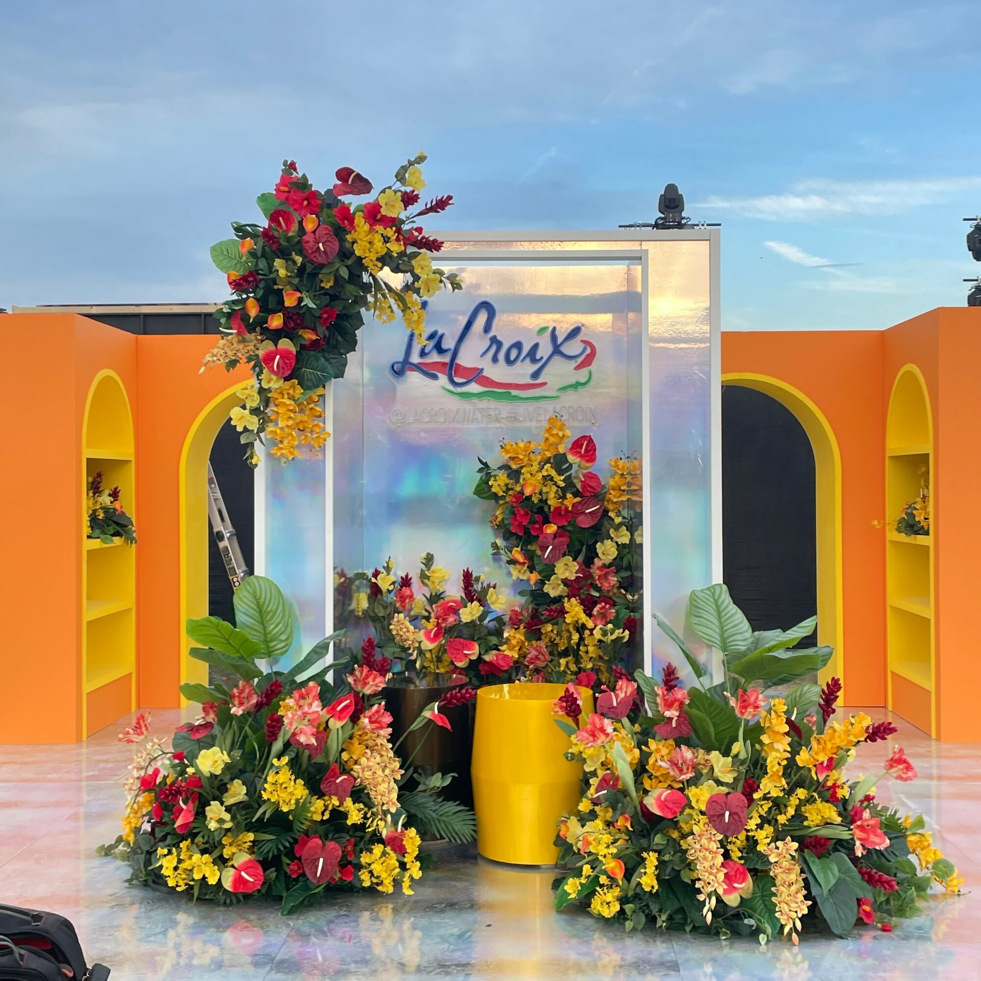 Colorful floral display with yellow shelves and a sign that reads 'La Croix' in the background, outdoors under a blue sky.