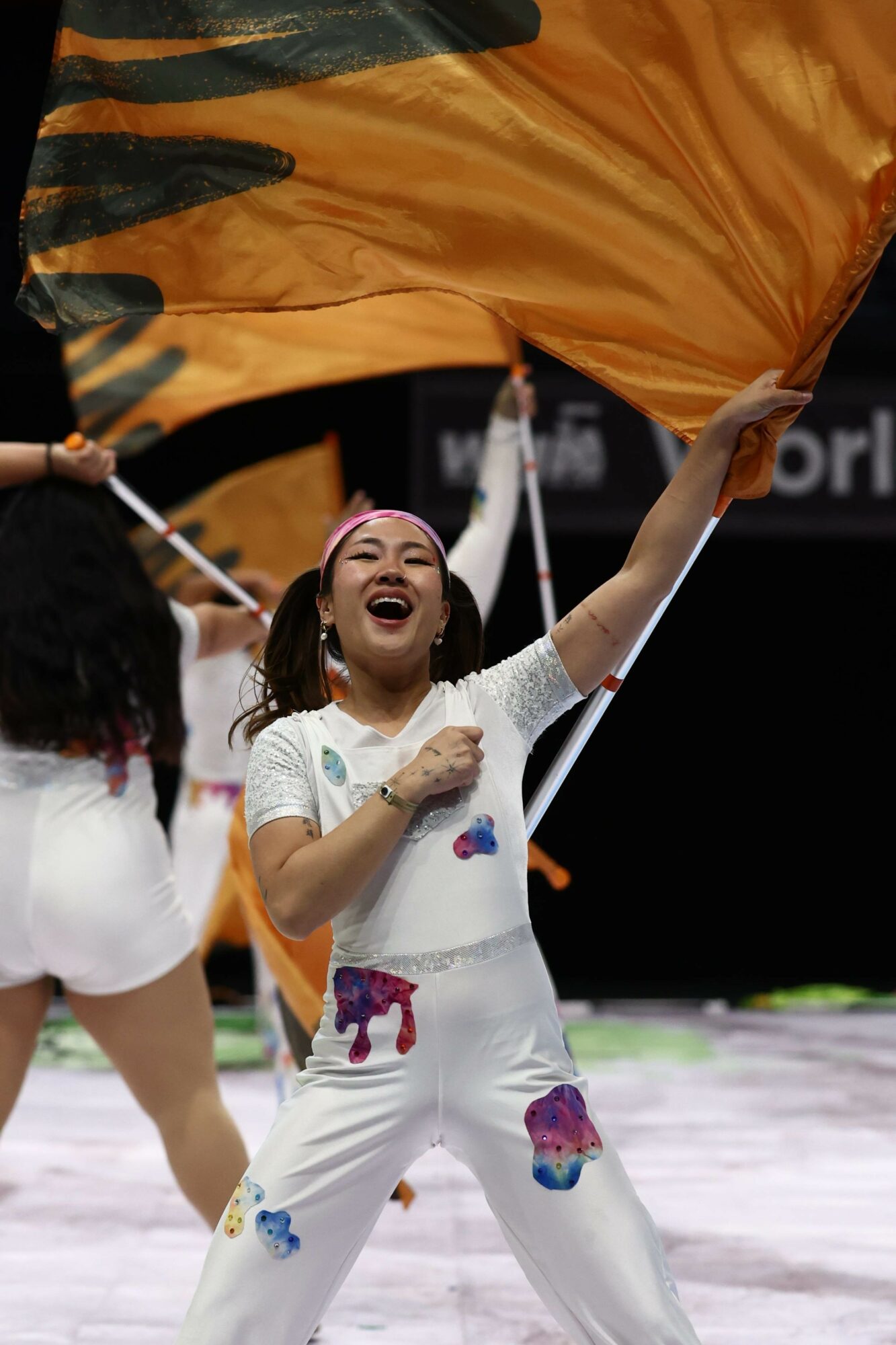 Young girl smiling and holding a large orange and black flag during a performance.