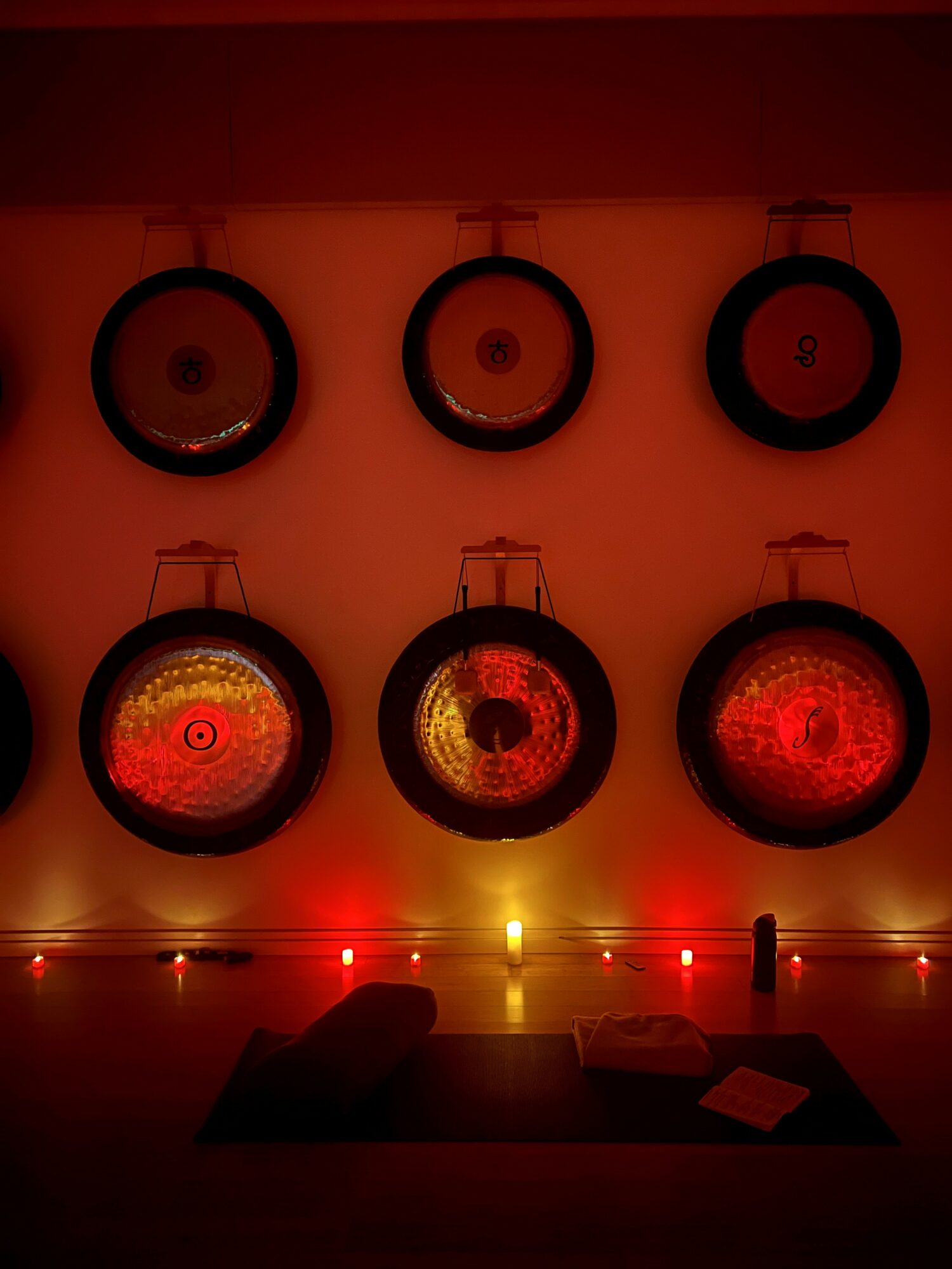 Six circular objects mounted on a wall, illuminated with red and yellow lights, arranged in two rows of three.