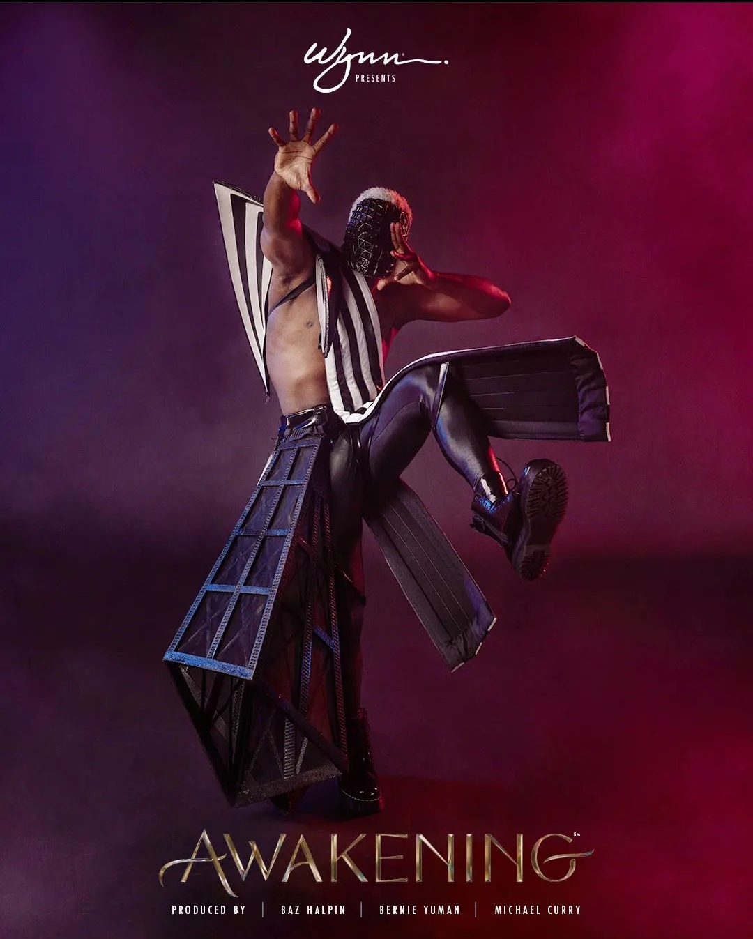 Person in black outfit with striped top, striking a pose on stage with colorful lighting.
