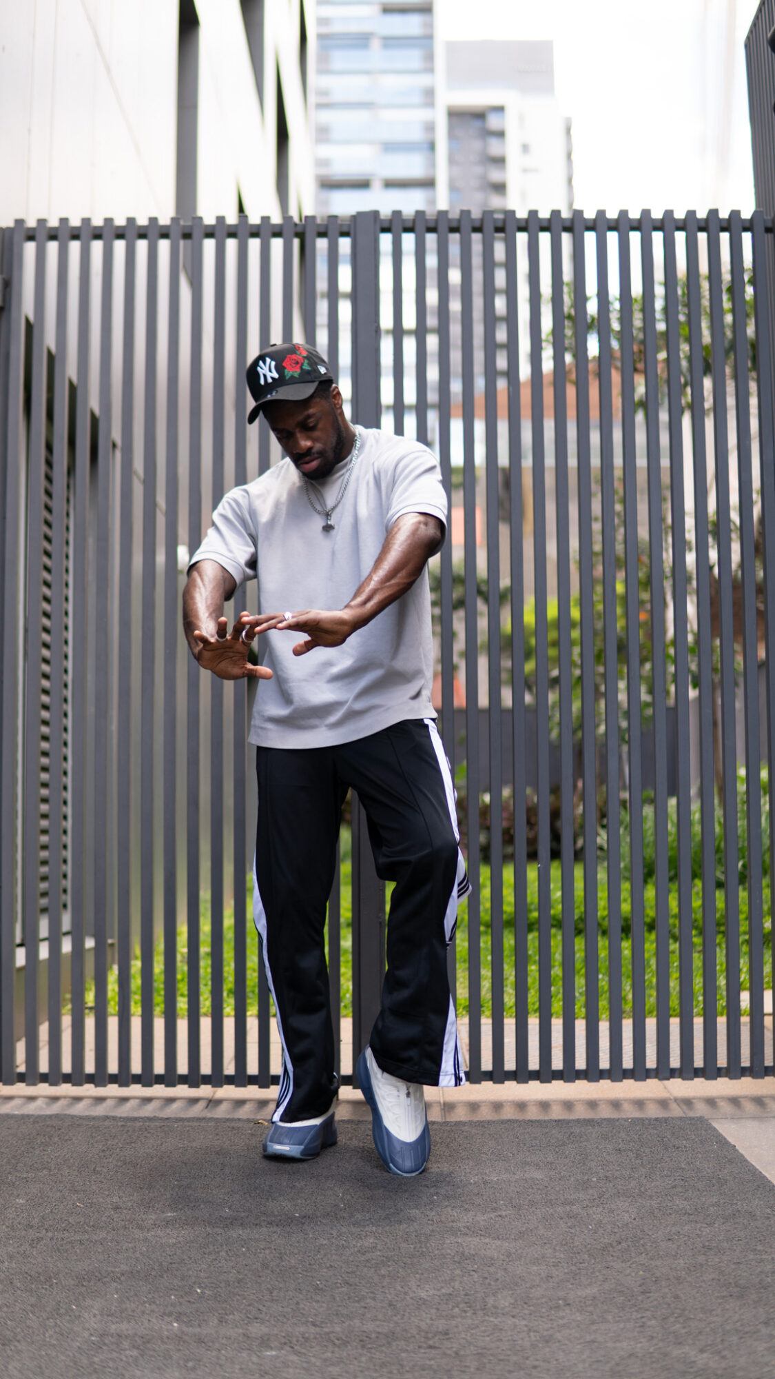 Person standing in front of a metal fence, looking at their phone, with buildings in the background.