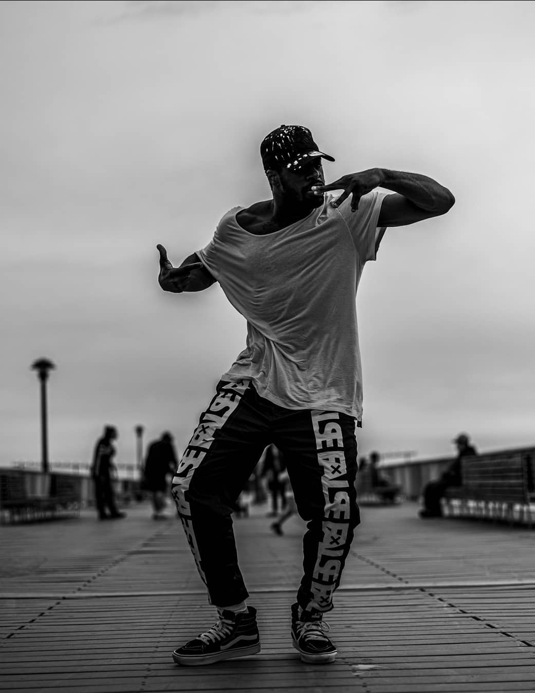 Person dancing outdoors on a wooden platform with a cloudy sky background.