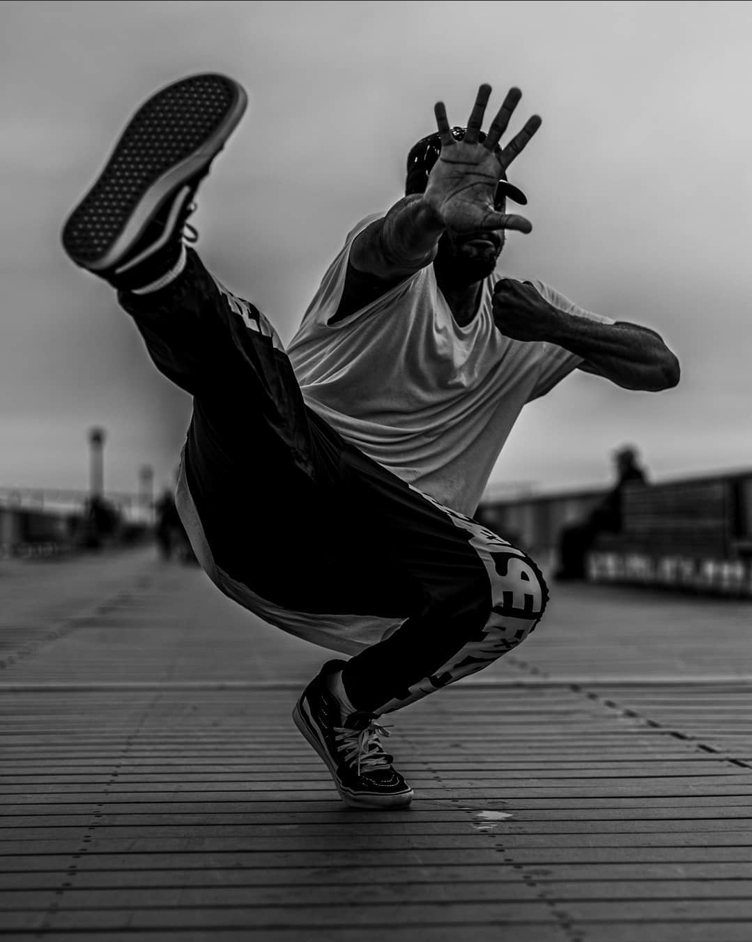 Person performing a dynamic move on a wooden surface outdoors, with one leg extended and arms outstretched.