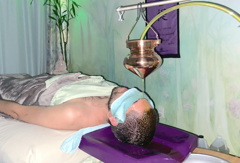 Person lying on bed with head under a medical device, in a room with green walls and plants.