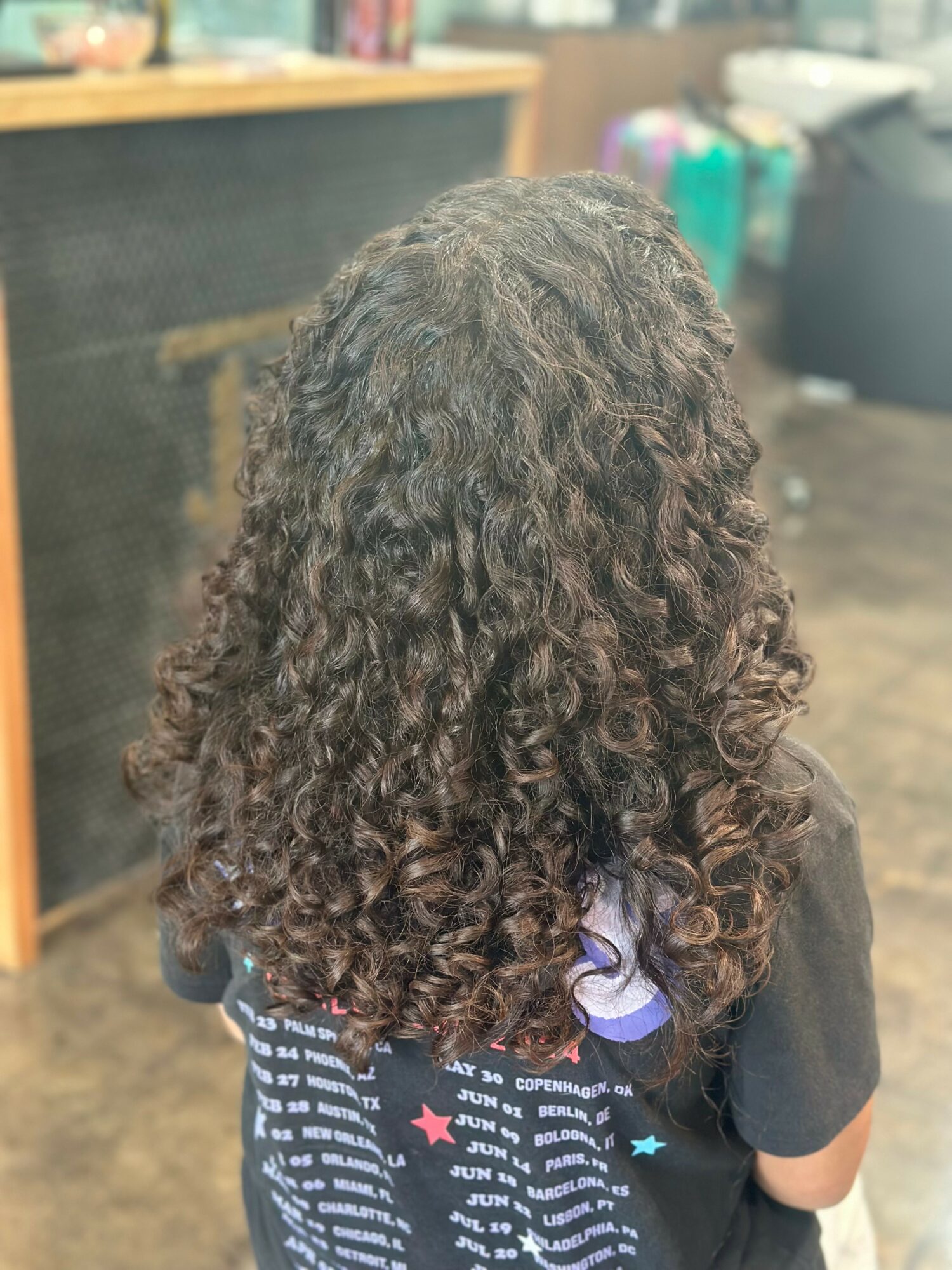 Back view of person with long, curly hair in a room with shelves and colorful items.