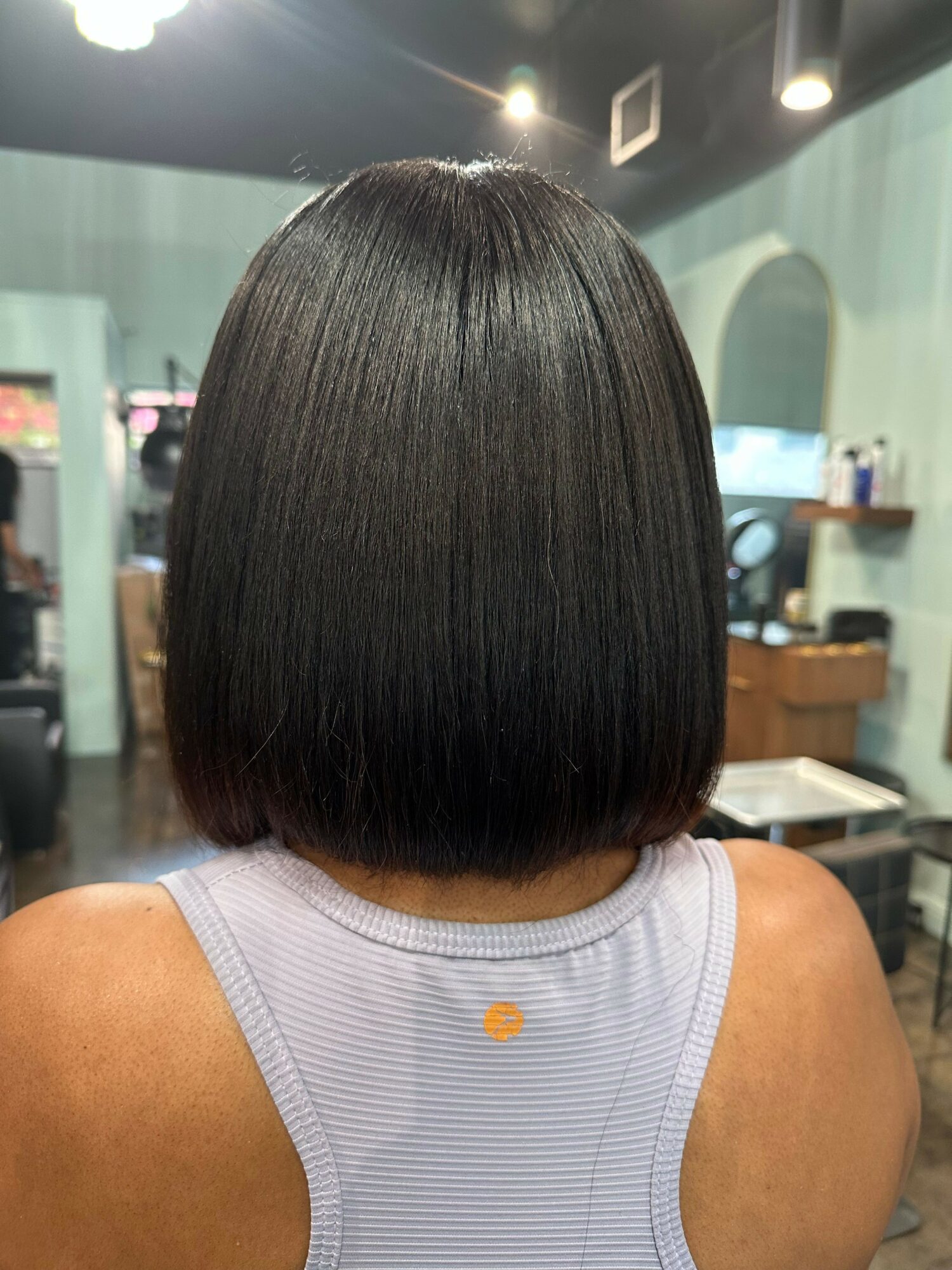 Back of a person's head with a straight, chin-length bob haircut in a salon setting.