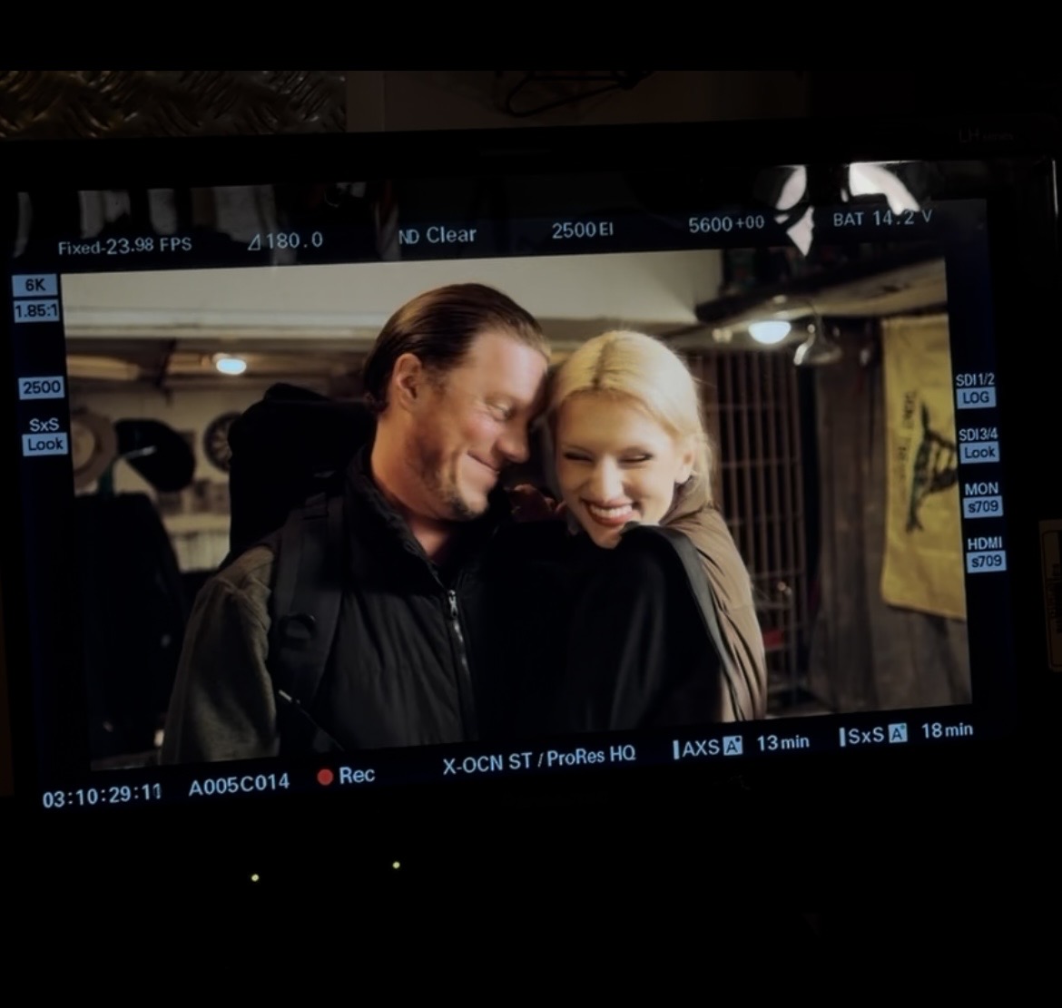 Two people smiling and hugging in a dimly lit indoor setting.