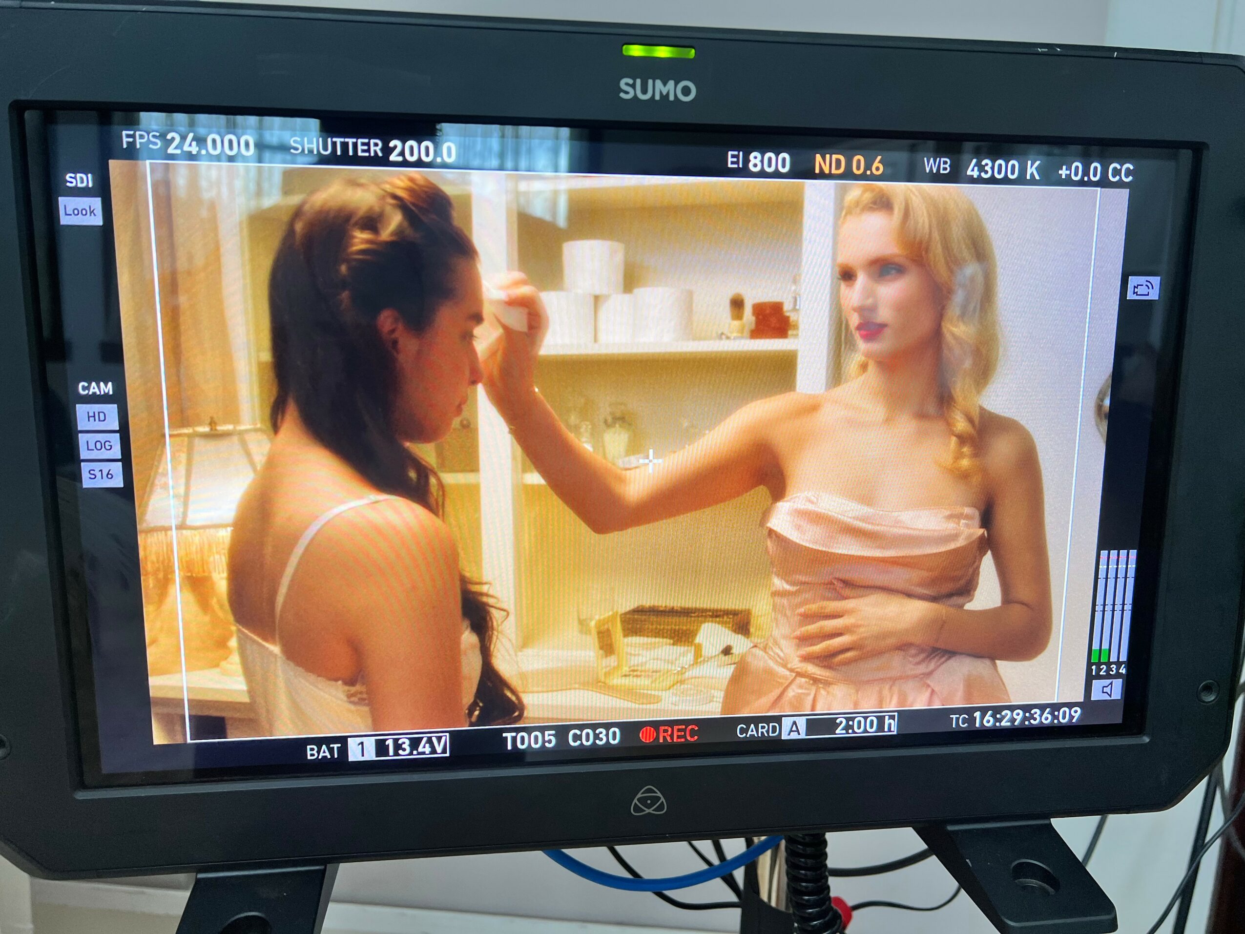 Two women in a kitchen, one touching the other's face, shelves with dishes in background.