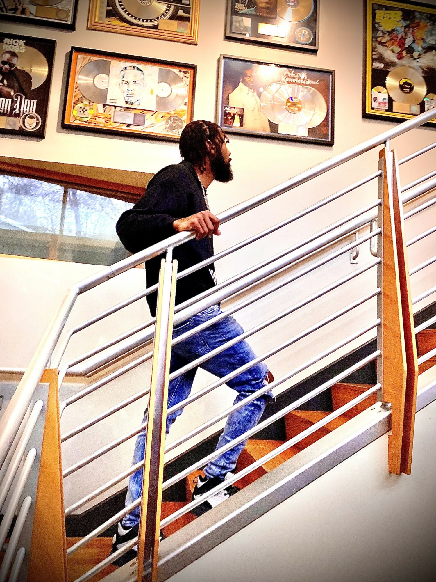 Man with beard and glasses walking up a staircase with framed artwork on the wall behind him.
