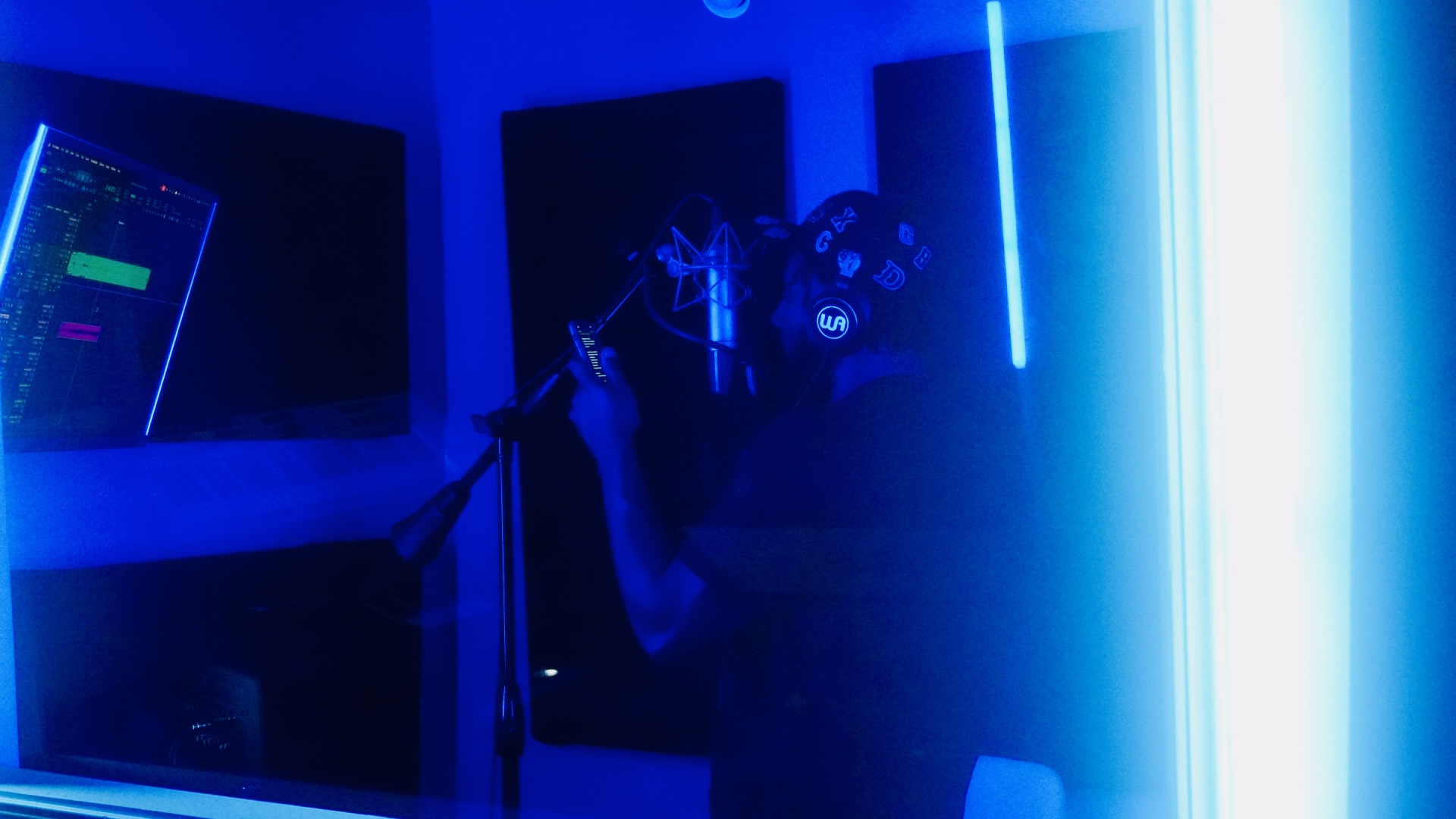 Person holding headphones in a dark room illuminated by blue neon lights, with computer screens visible.