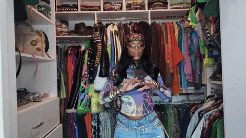 Person standing in a walk-in closet with colorful clothes hanging on racks behind them.