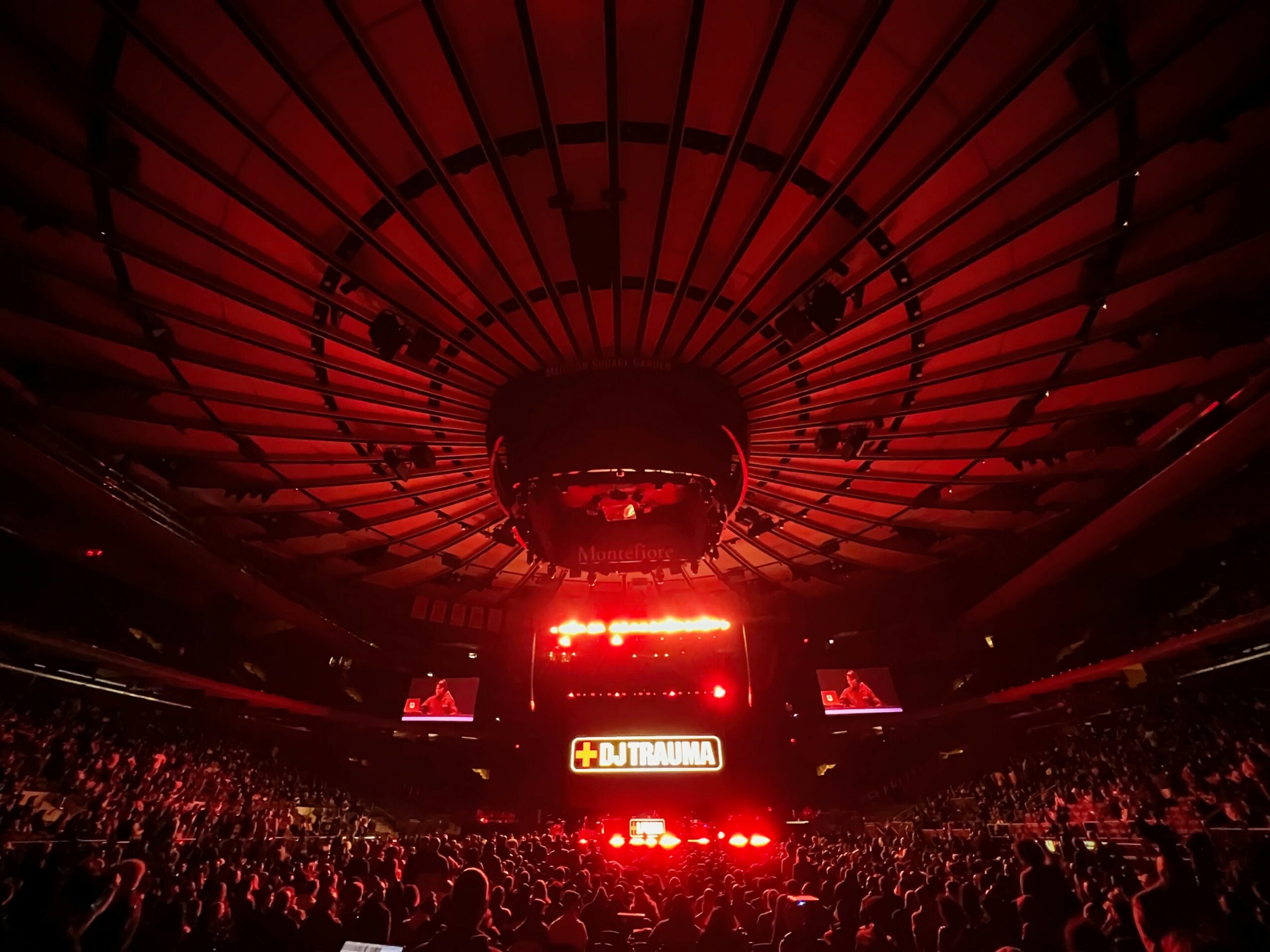Large indoor arena filled with audience watching a brightly lit stage with screens and lights.