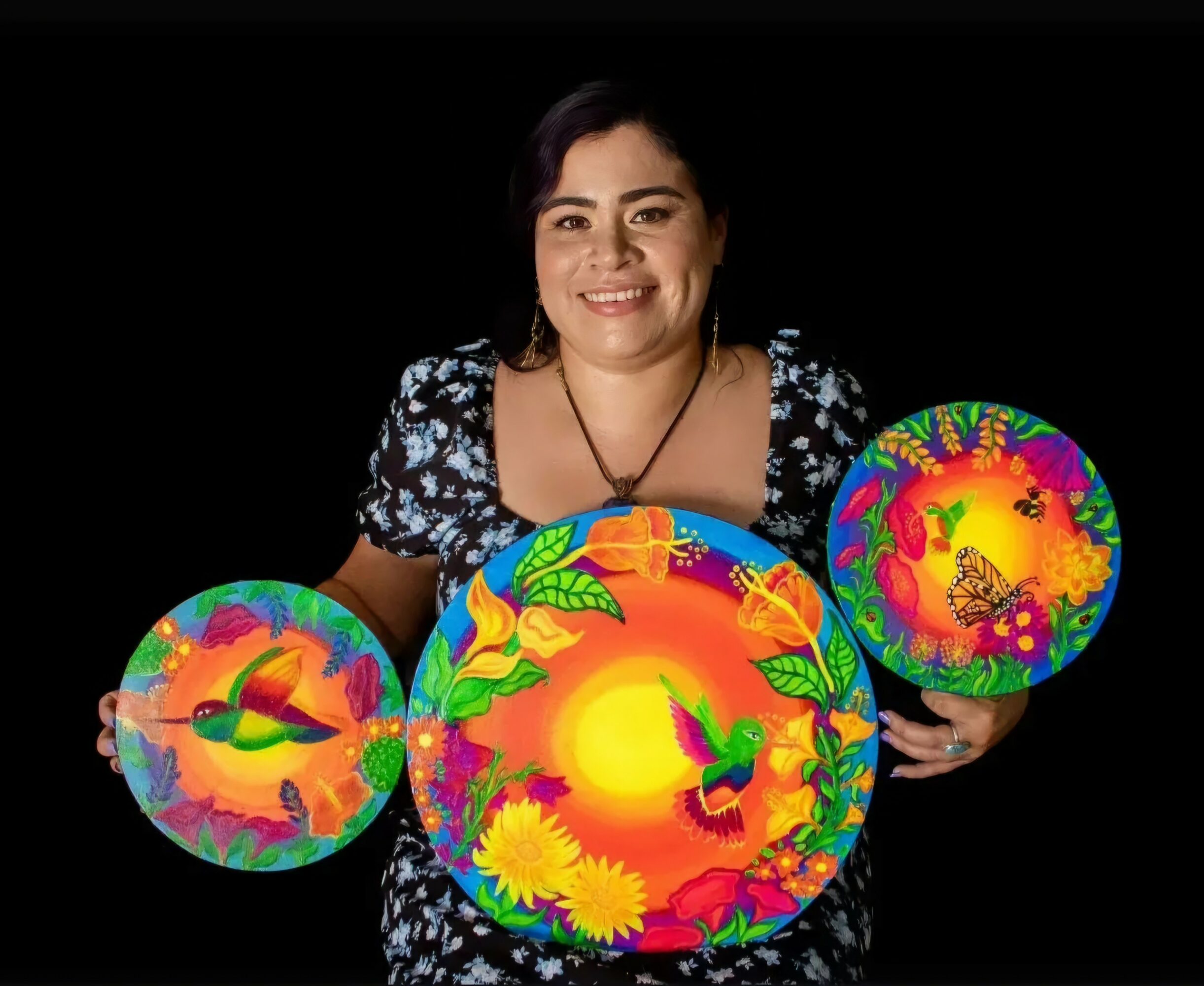 Woman holding three colorful, illuminated spherical objects with floral and nature patterns, smiling at the camera.