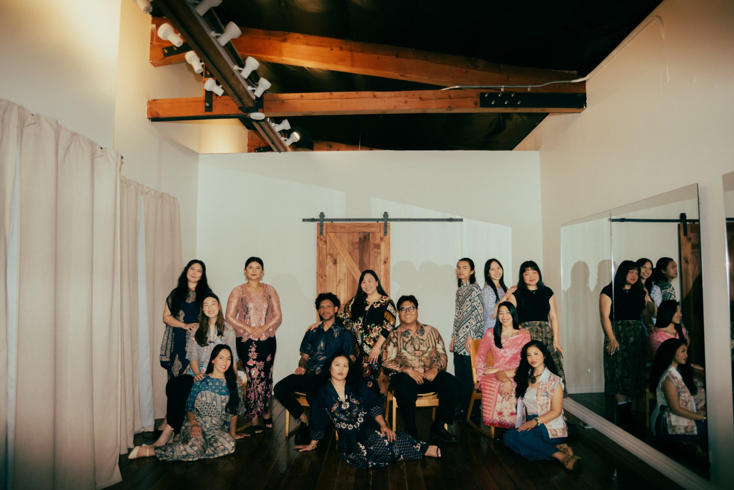 Group of people posing in a room with white curtains and a wooden door, some sitting and some standing.