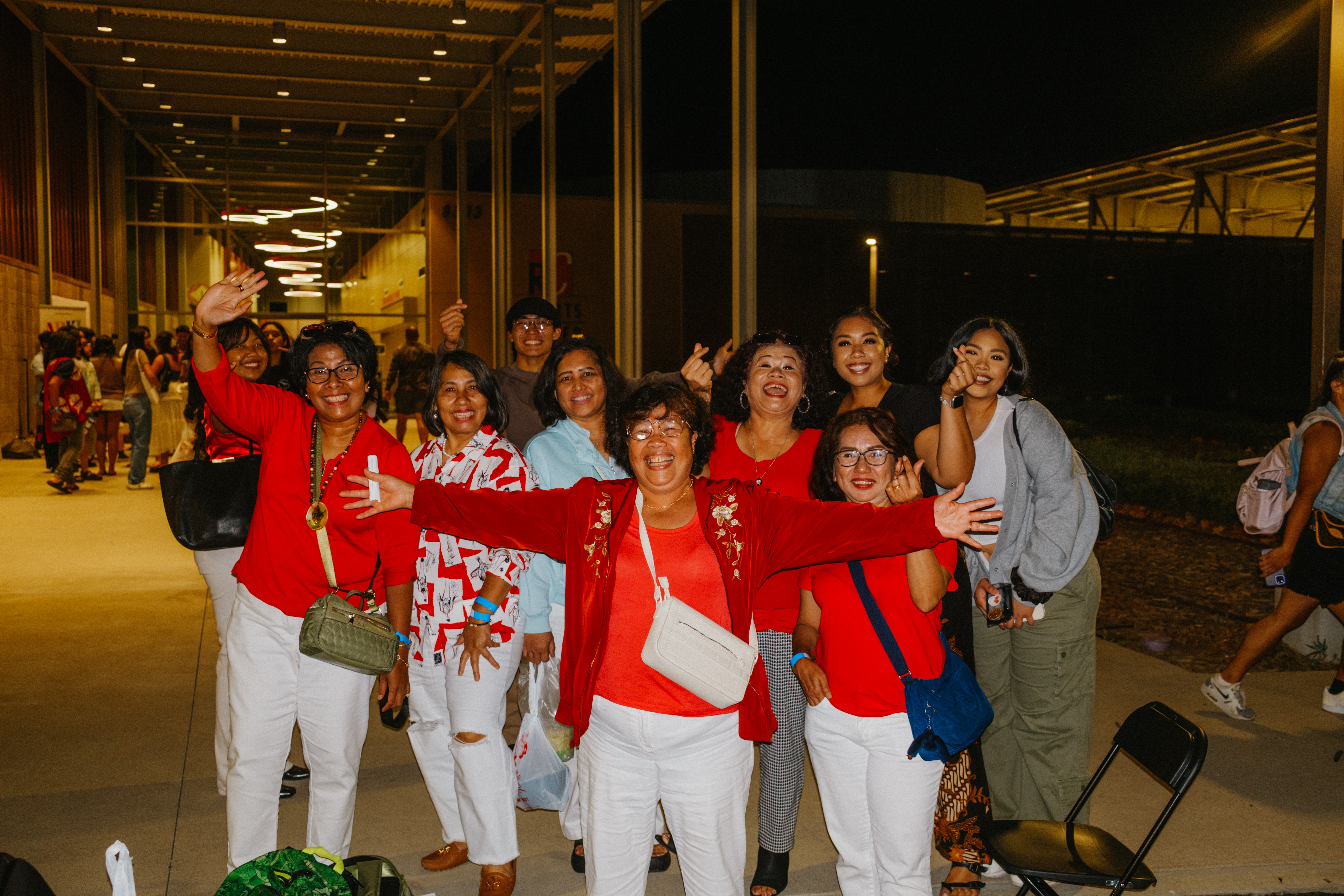 Group of women smiling and posing together outdoors at night, some with arms raised, in a well-lit area.