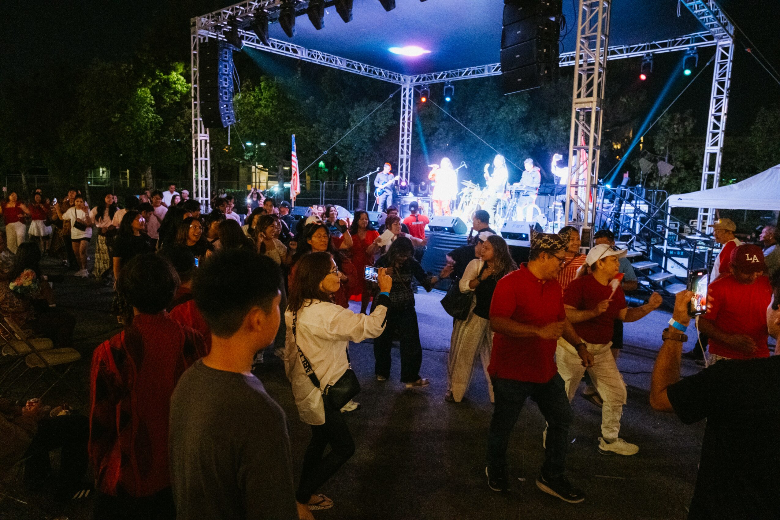 People dancing outdoors at night near a stage with bright lights and musical performance.