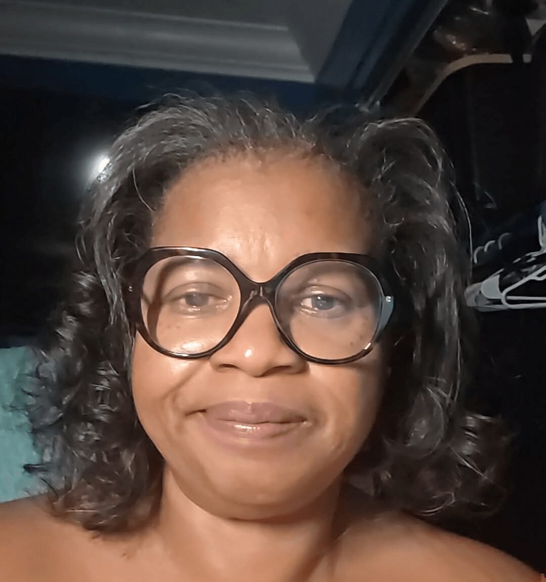 Woman with glasses and curly hair smiling at the camera.