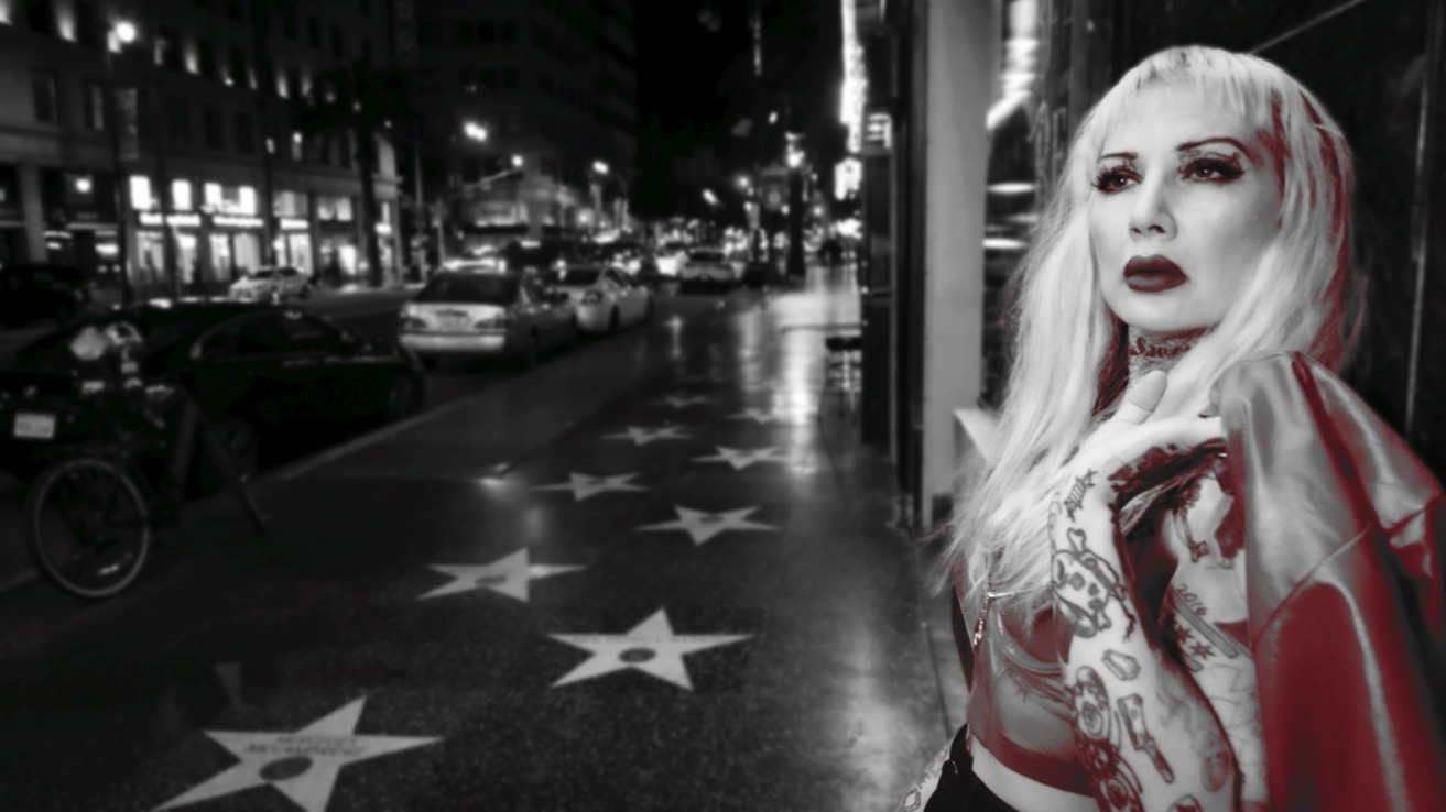 Woman with long blonde hair and red lipstick standing on a star-lined city street at night.