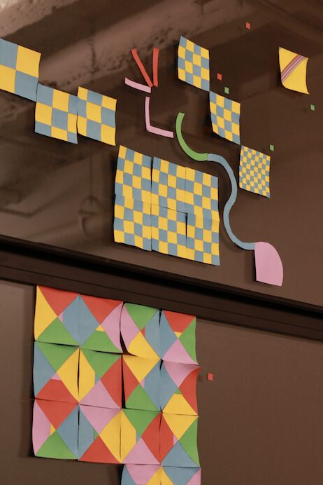 Colorful geometric paper art with checkered and diamond patterns, arranged on a dark surface.