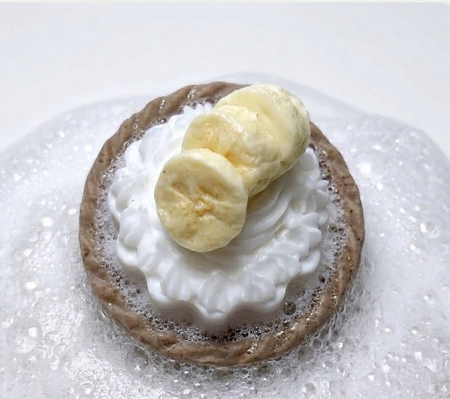 Chocolate cookie topped with whipped cream and banana slices, on a clear plate with powdered sugar.