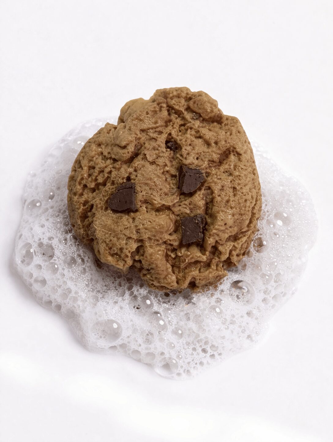 Chocolate chip cookie on soapy surface with bubbles, plain white background.