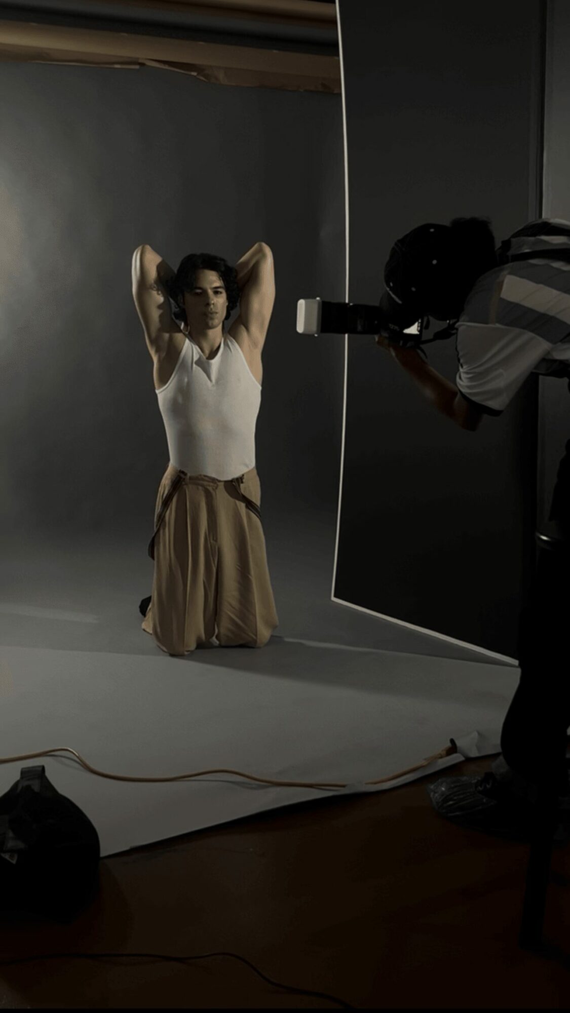 Person sitting on the floor with hands behind head in a photography studio, with a photographer taking pictures.