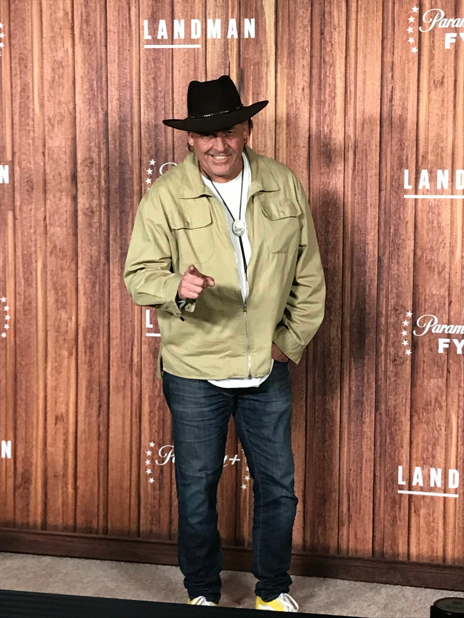 Man in a hat and jacket standing in front of a wooden backdrop with logos.