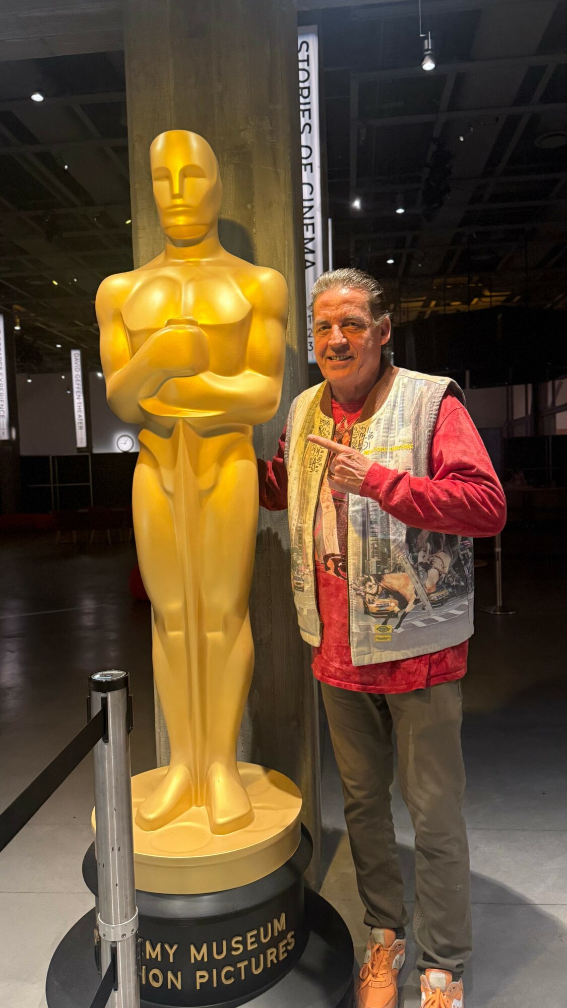 Person standing next to a large golden Oscar statue inside a museum or exhibition space.